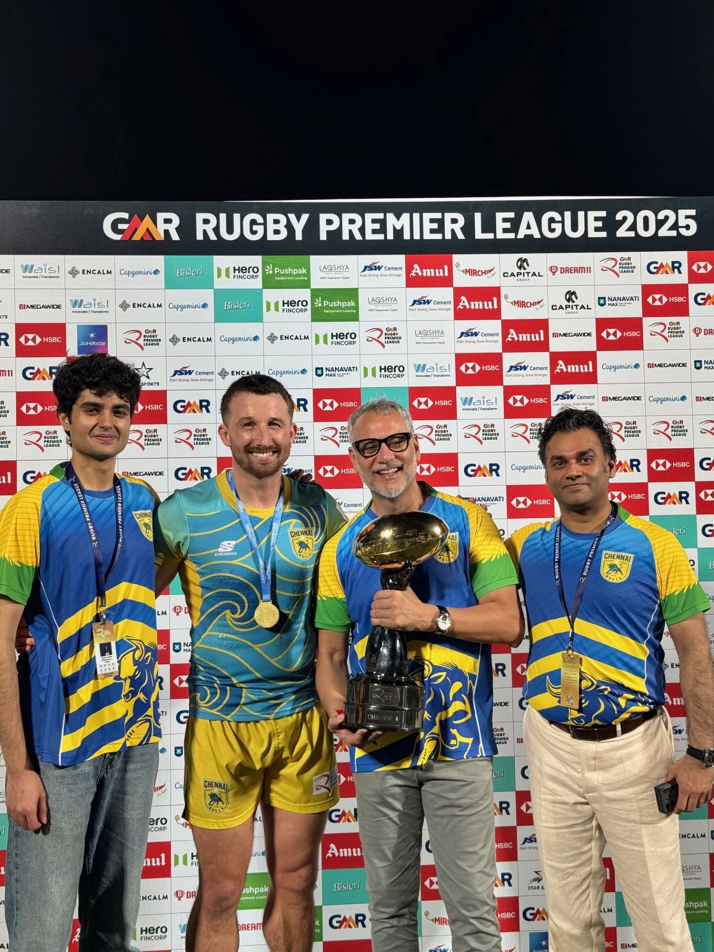 Four men in Chennai team jerseys stand smiling with Dipen Rughani holding a trophy at the Rugby Premier League 2025 backdrop.