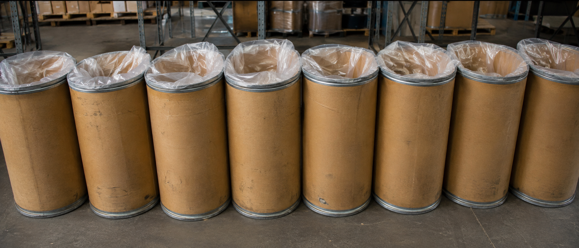 Row of fiber drums with liner bags visible at the open top, in a warehouse
