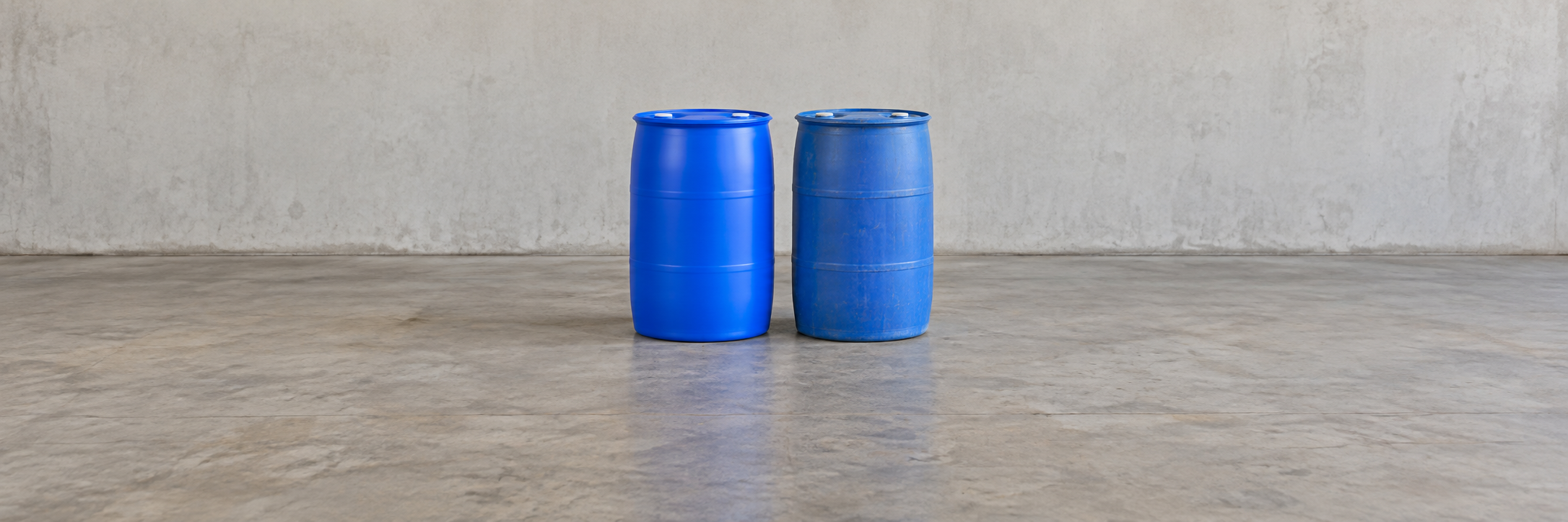 A new plastic drum standing next to a used reconditioned plastic drum on a concrete floor