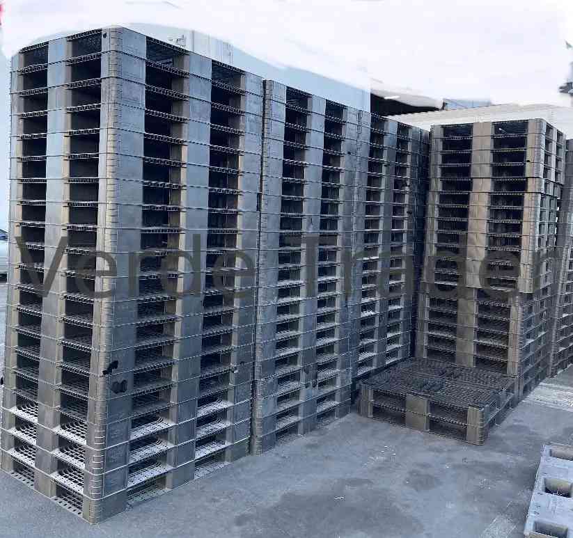 Forklift moving stacked plastic pallets near a warehouse loading dock