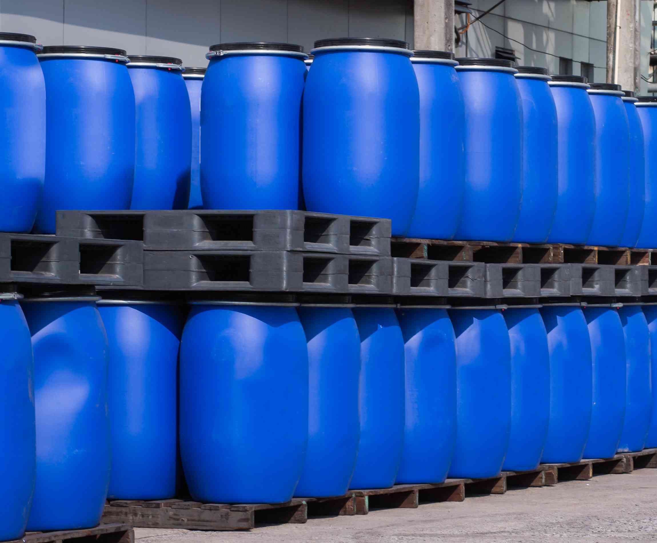 Photo of 55-gallon drums stacked on pallets outside a warehouse