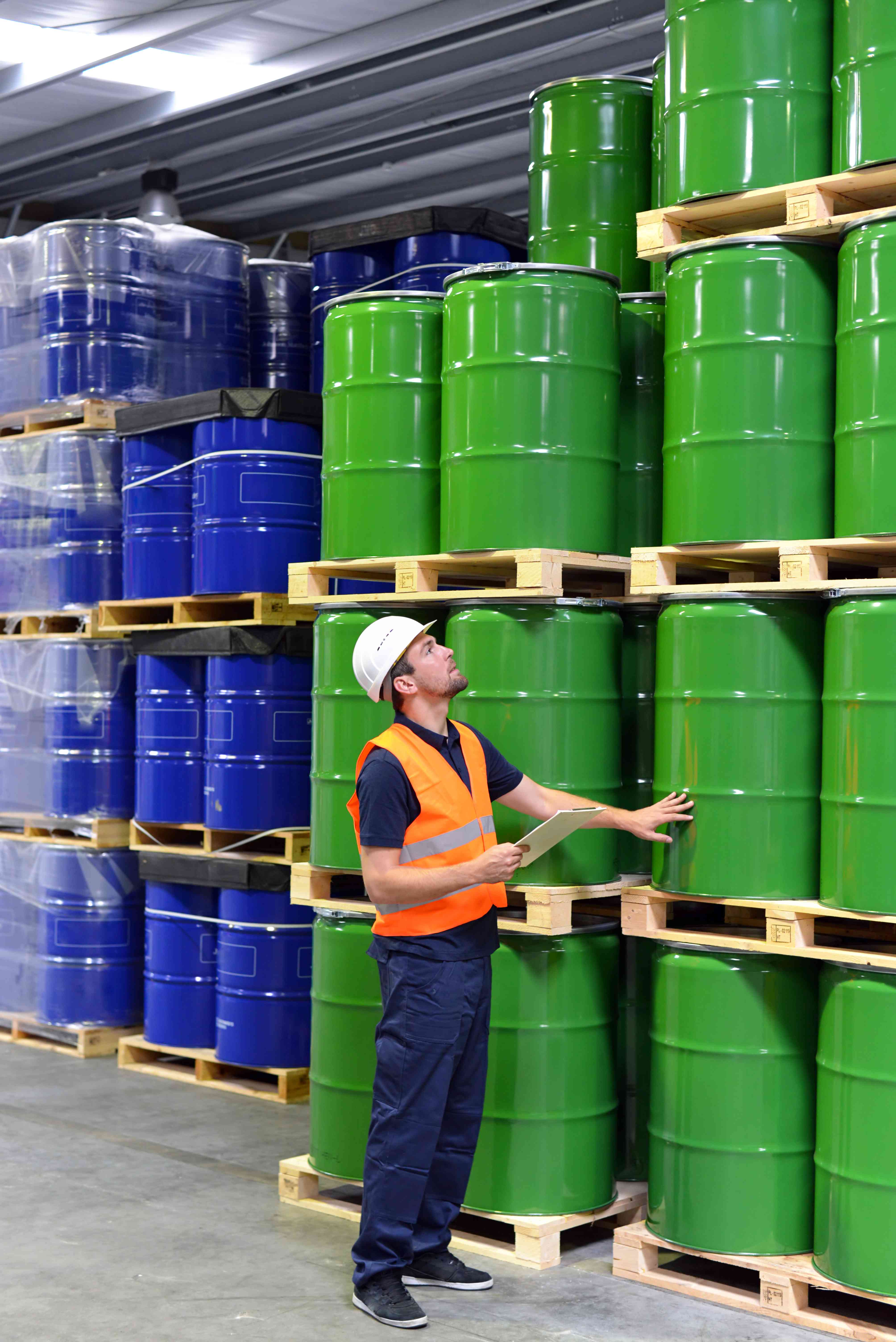 Warehouse employee inspecting green steel drums on pallets.
