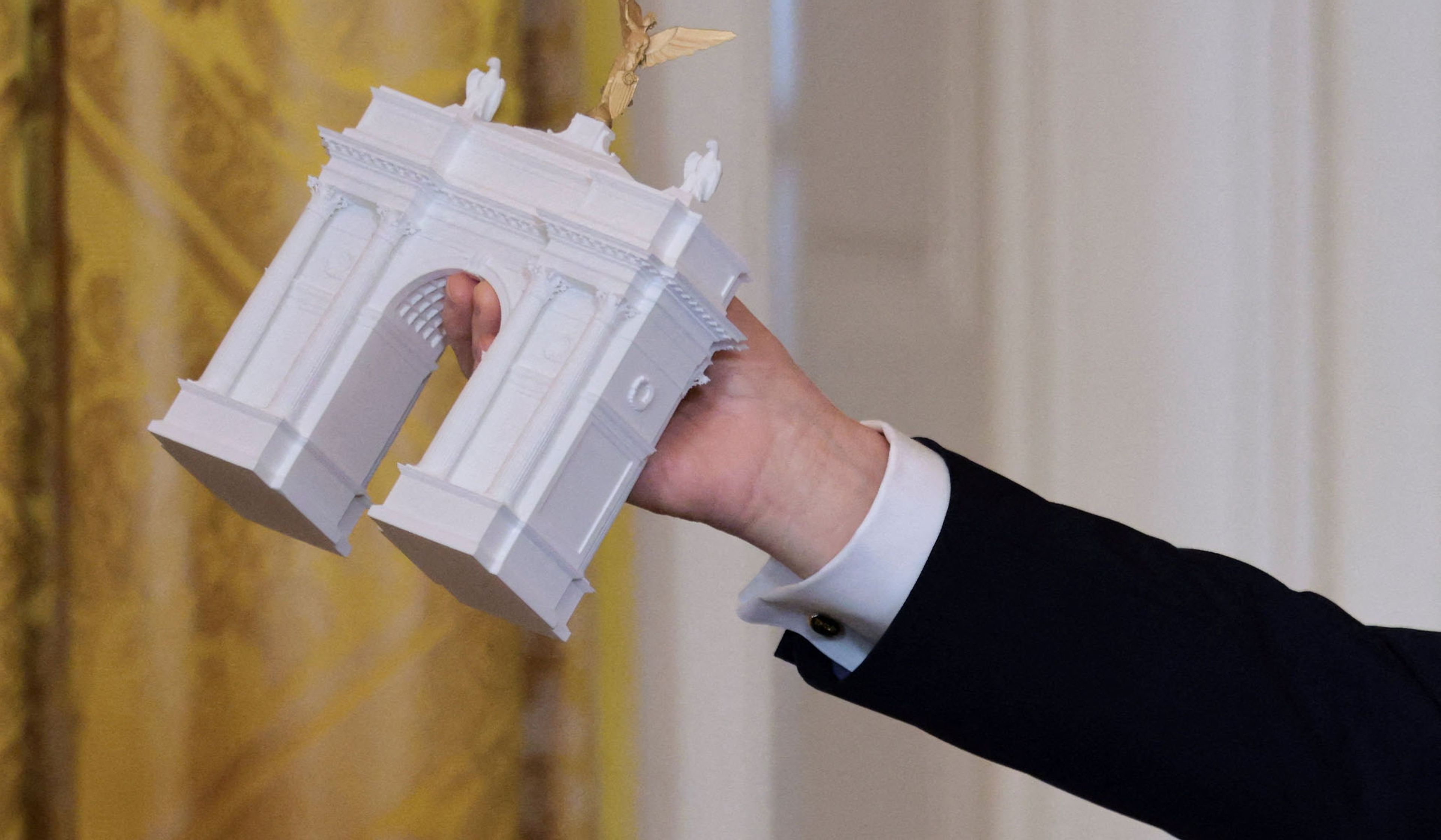President Donald Trump holds a model of an arch monument during a ballroom dinner in the East Room at the White House in Washington, D.C., October 15, 2025.