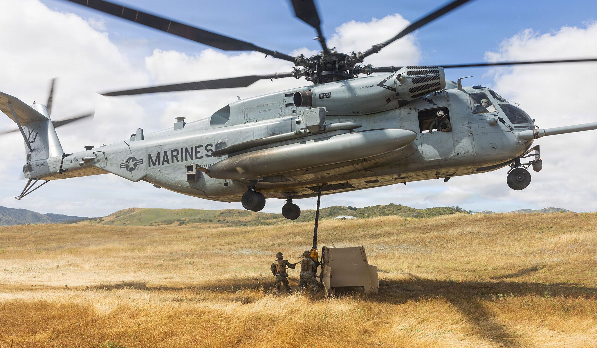 U.S. Marine Corps Corporal Naquis Williams, Private First Class Matthew Reich, and Corporal Luke Greene, all logistics specialist with First Distribution Support Battalion, Combat Logistics Regiment One, First Marine Logistics Group, attach a steel target to a CH-53E Super Stallion assigned to the “Warhorse” of Heavy Helicopter Squadron HMH-465, Marine Aircraft Group MAG-16, Third Marine Aircraft Wing, during helicopter support team training at Marine Corps Base Camp Pendleton, Calif., April 21, 2026.