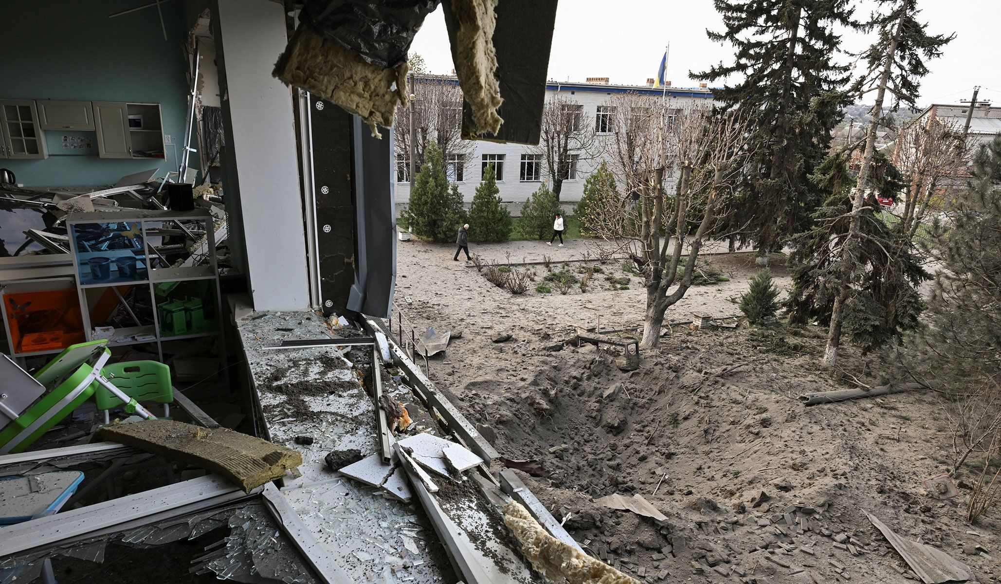 Employees walk next to a crater that appeared at a compound of a school after a Russian air strike on the outskirts of Zaporizhzhia, Ukraine, April 9, 2026.