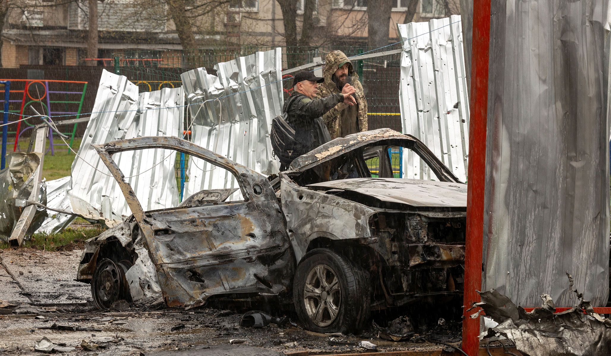 Men stand next to a burned car at the impact site of a Russian drone in a residential neighborhood in Vyshneve, outside Kyiv, Ukraine, April 3, 2026.