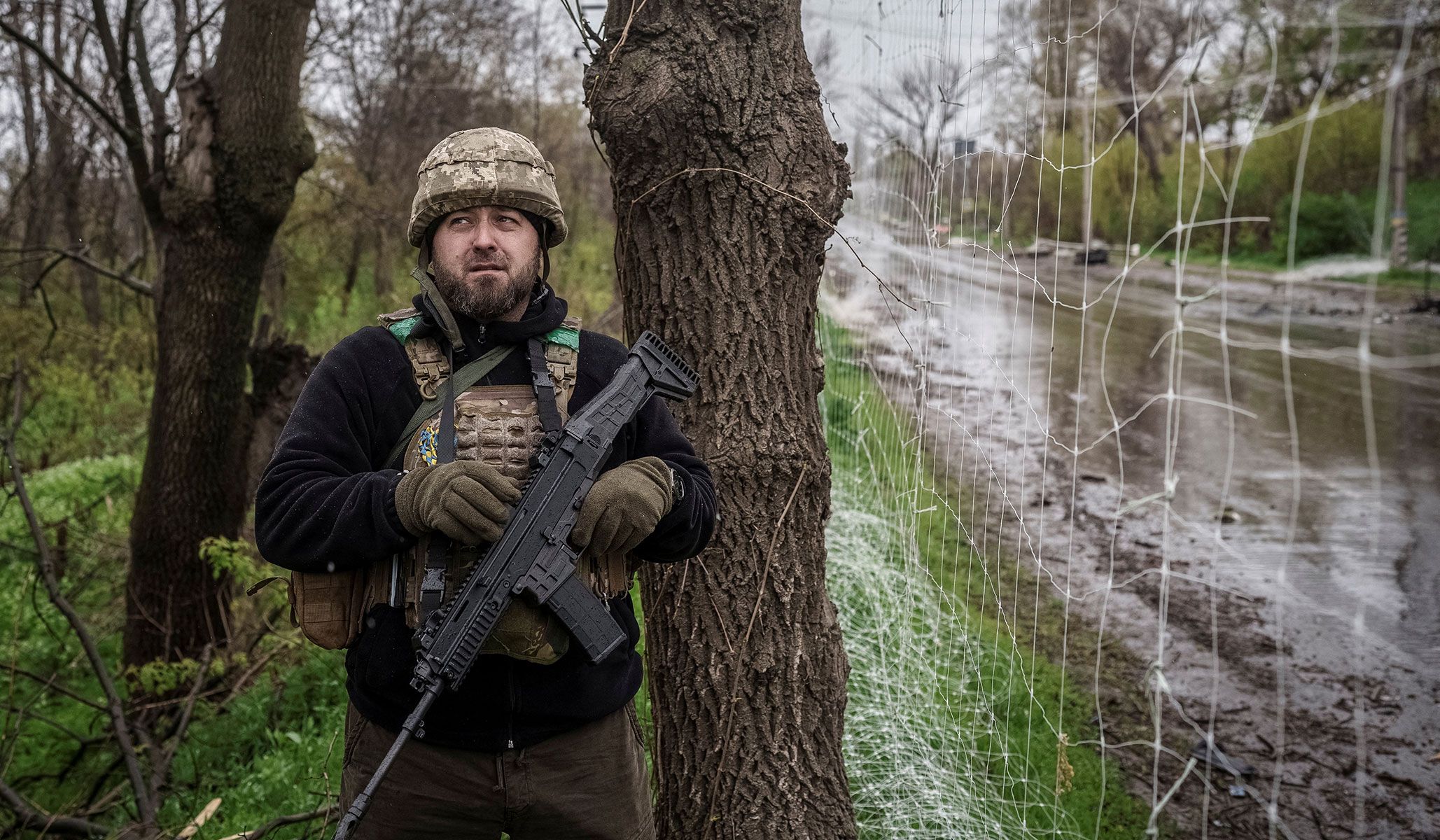 A serviceman of the 24th Separate Mechanized Brigade of the Ukrainian Armed Forces hides under trees as he observes the sky for Russian drones during a mission to protect streets in the frontline town of Druzhkivka, Donetsk Region, Ukraine, April 24, 2026.
