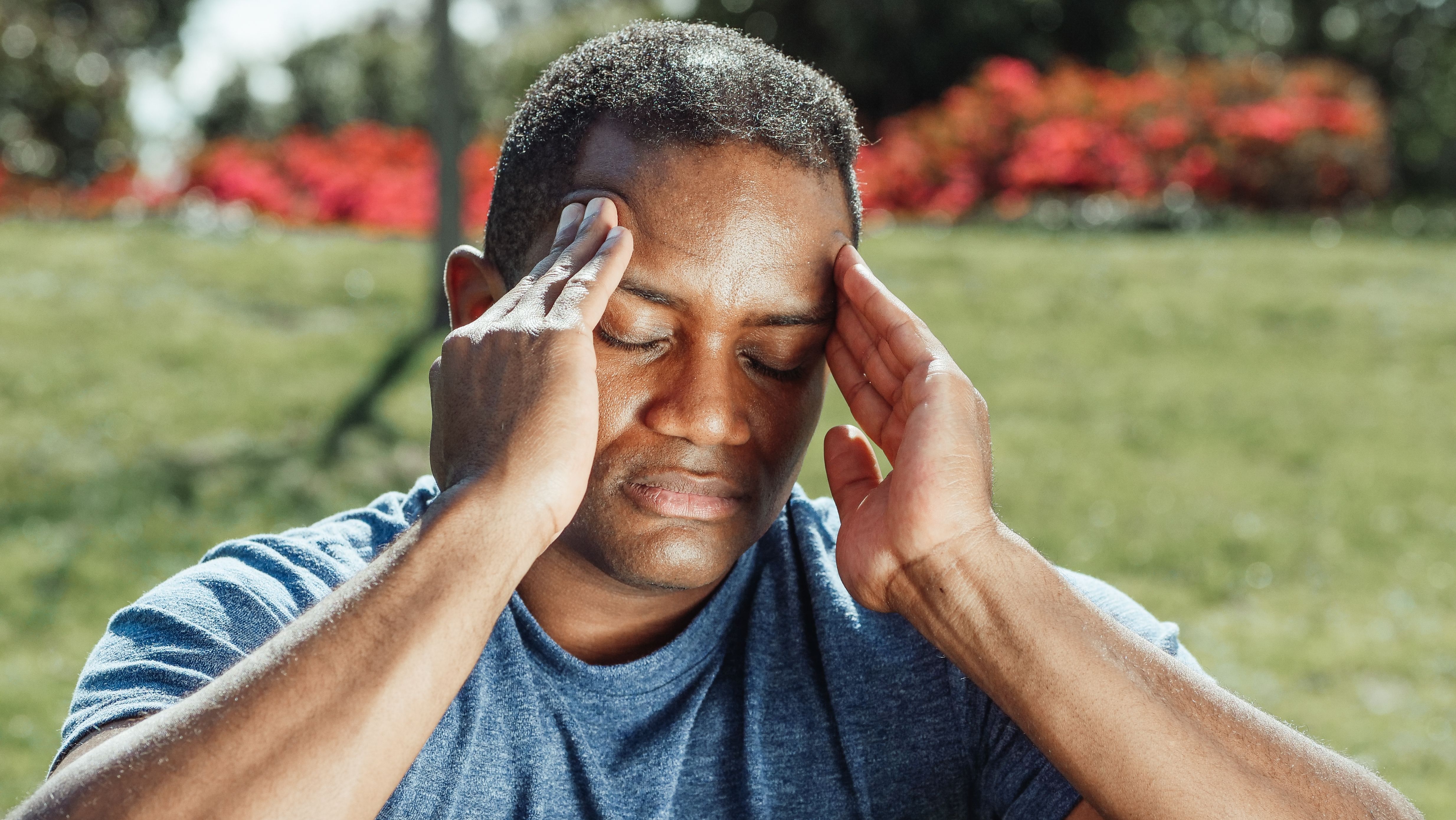Man outdoors holding his temples in pain from a headache, a common delayed symptom of a head injury after a Newark car accident.
