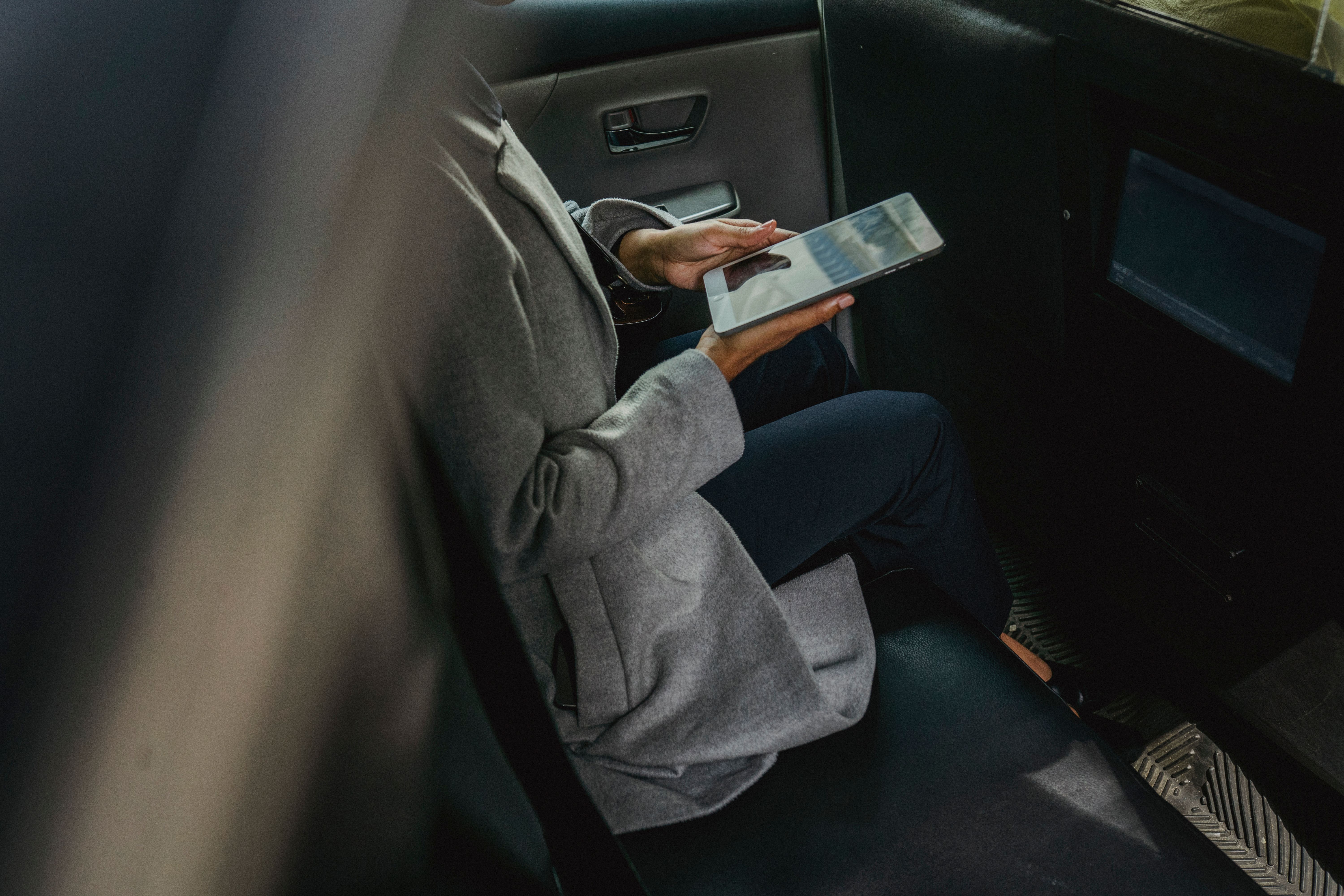 Passenger in business attire sitting in the back seat of a rideshare car using a tablet during a ride in New Jersey
