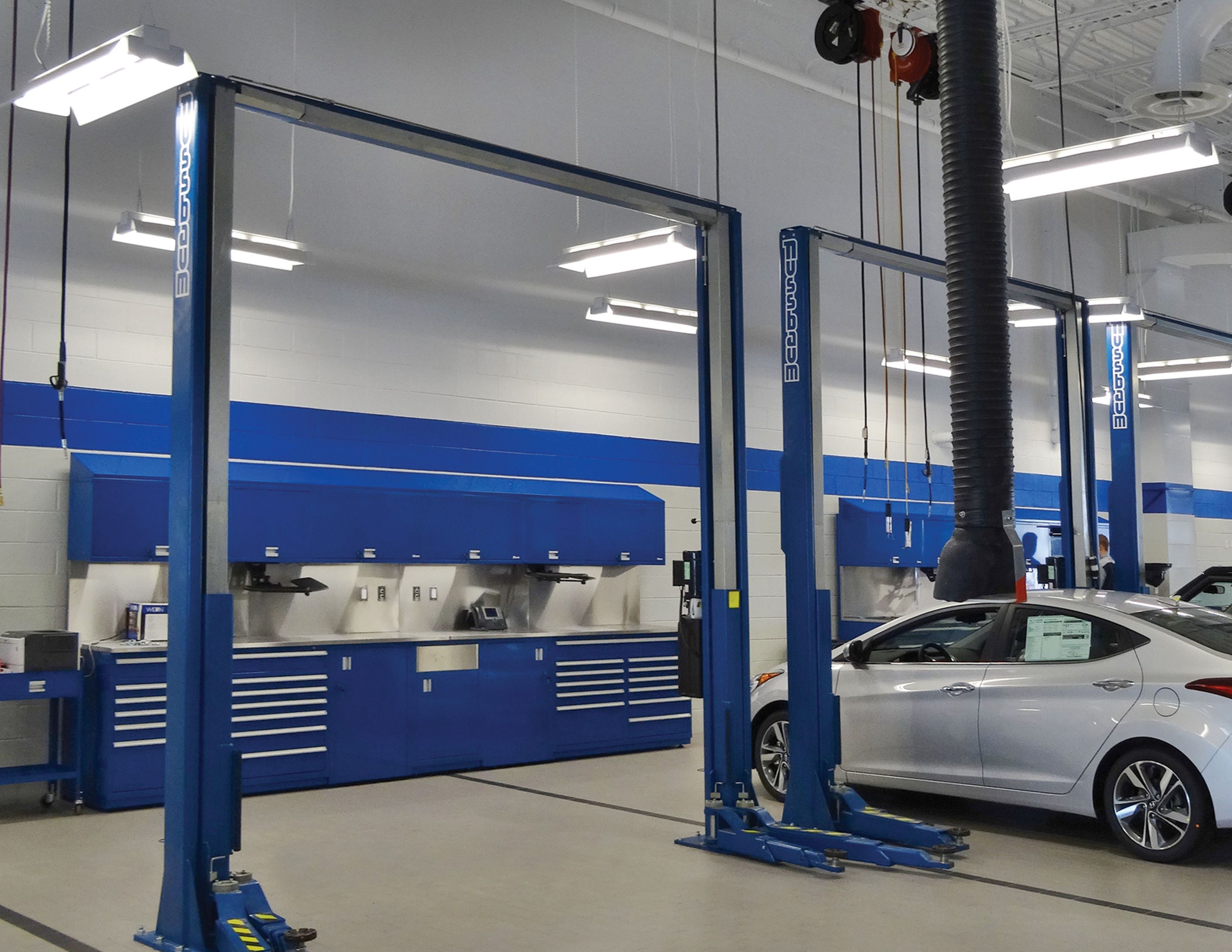 Service bay with blue vehicle lifts and matching blue workbenches and tool storage