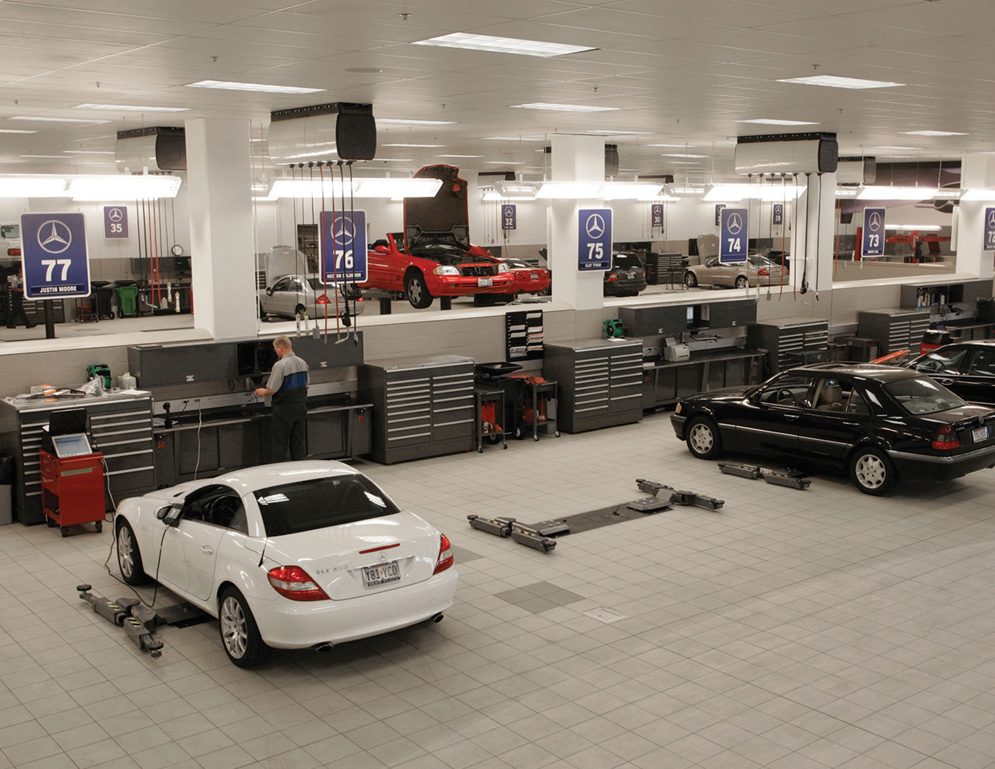Dealership service department with technicians at workstations and cars on the shop floor