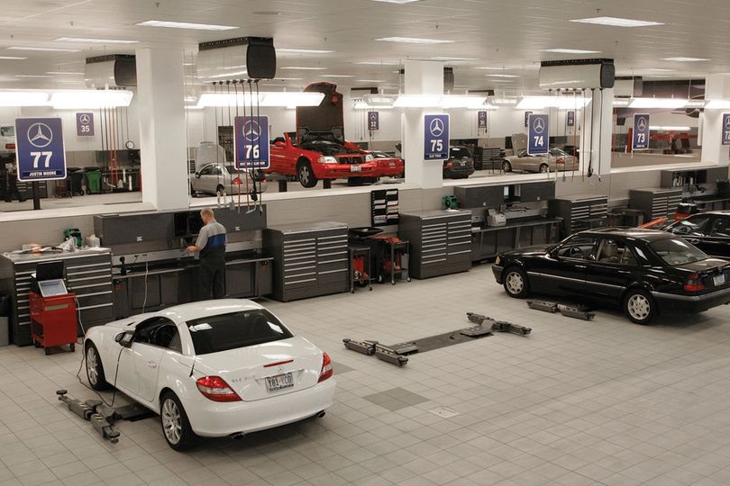 Dealership service department with technicians at workstations and cars on the shop floor