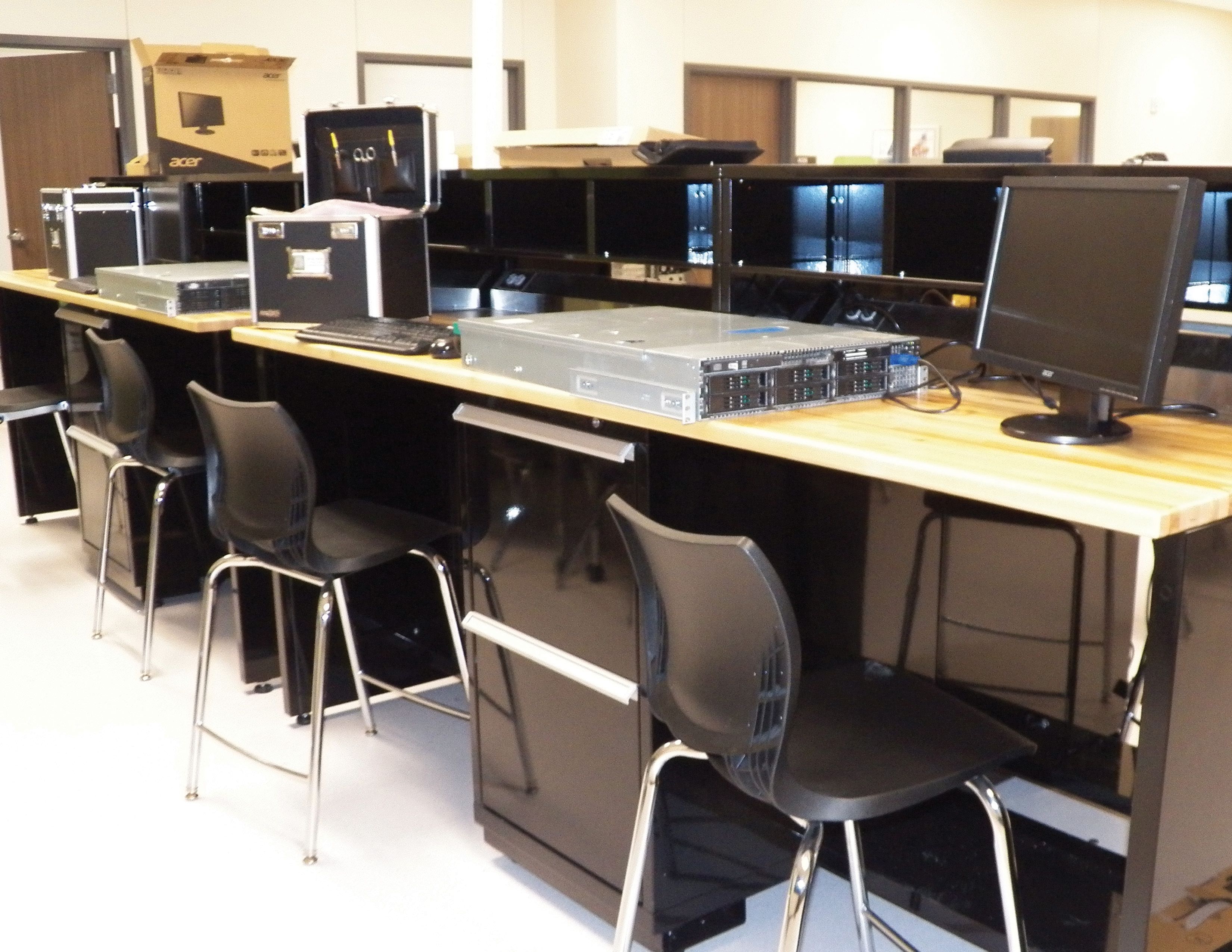 Classroom lab with wood-top steel workbenches, computer monitors and stools