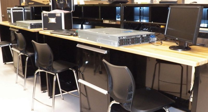 Classroom lab with wood-top steel workbenches, computer monitors and stools
