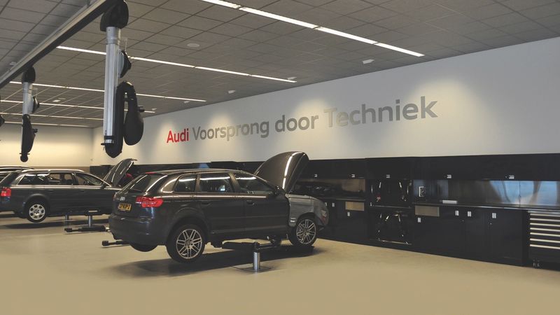 Dealership service hall with SUVs on lifts, overhead hose reels and a long run of black workbenches and cabinets