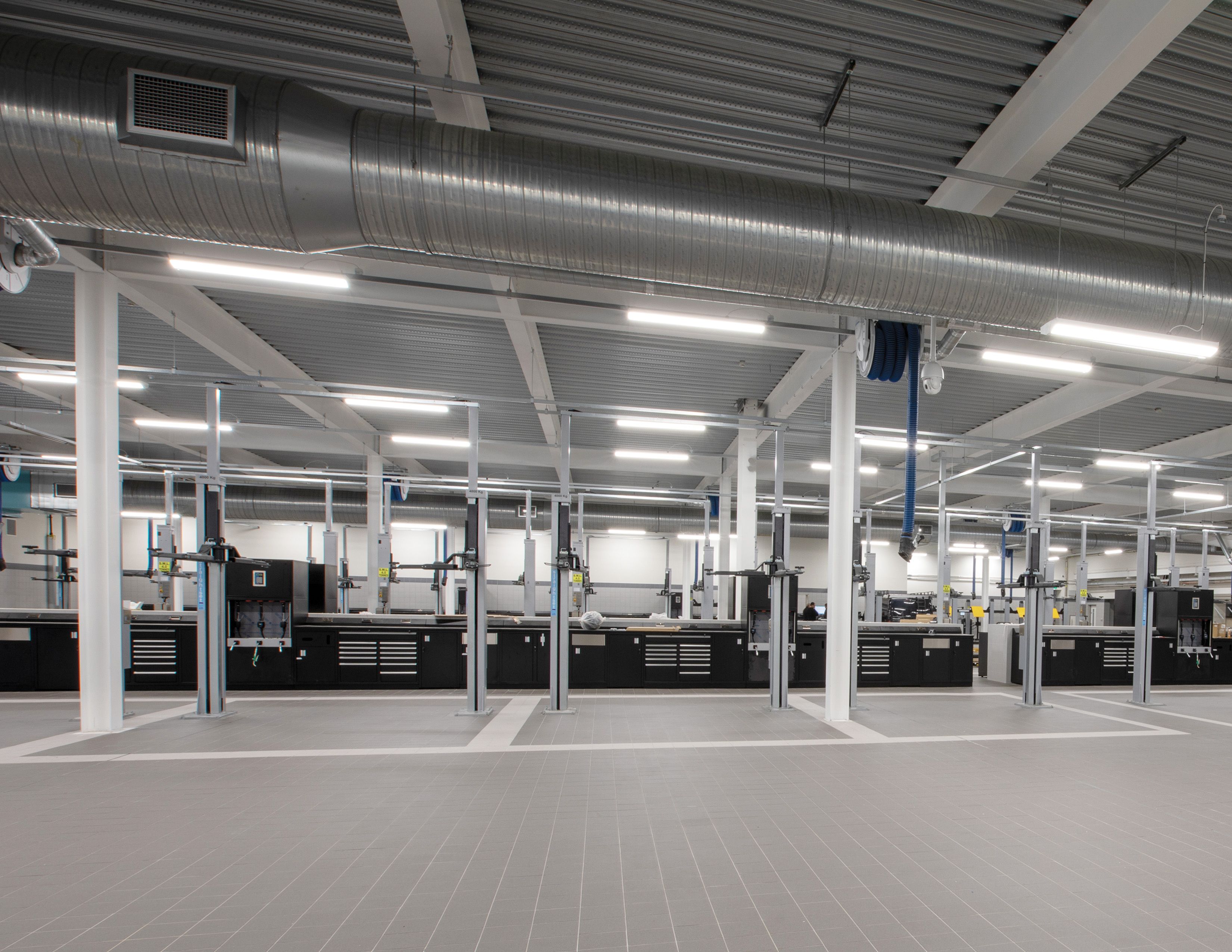 Large service hall with vehicle lifts and black workbench systems along the back wall