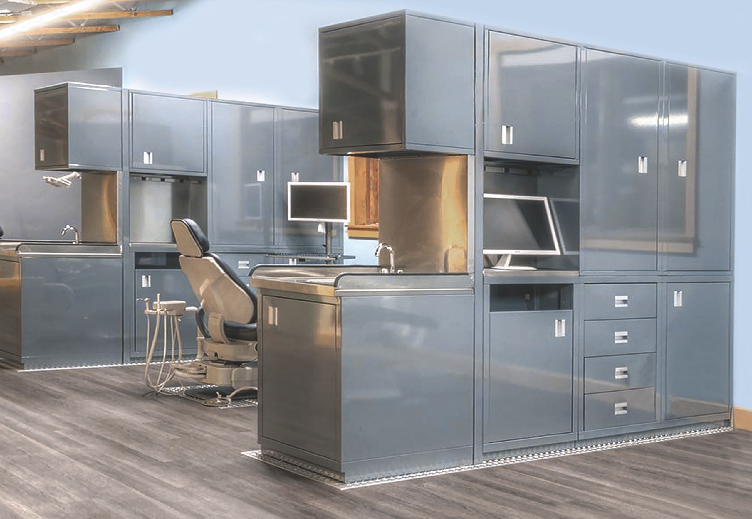 Grey steel cabinets, upper storage and a workstation with a monitor beside an exam chair