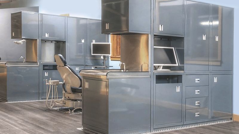 Grey steel cabinets, upper storage and a workstation with a monitor beside an exam chair