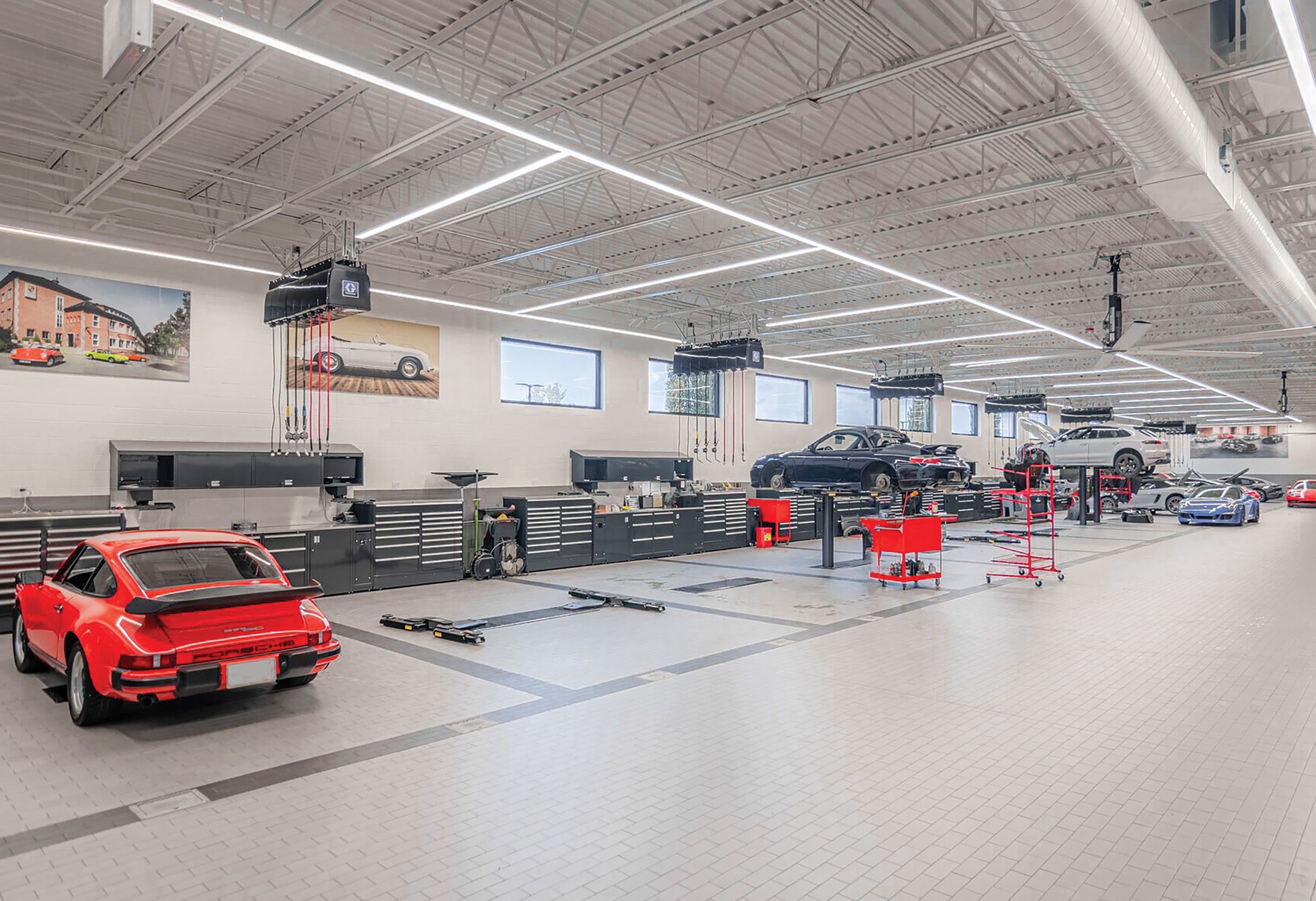 Bright dealership service bay with a red classic sports car and rows of steel workbenches and tool storage along the wall