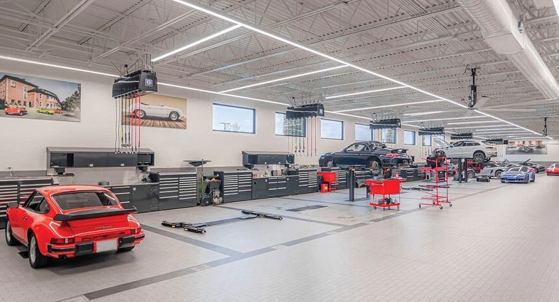 Bright dealership service bay with a red classic sports car and rows of steel workbenches and tool storage along the wall
