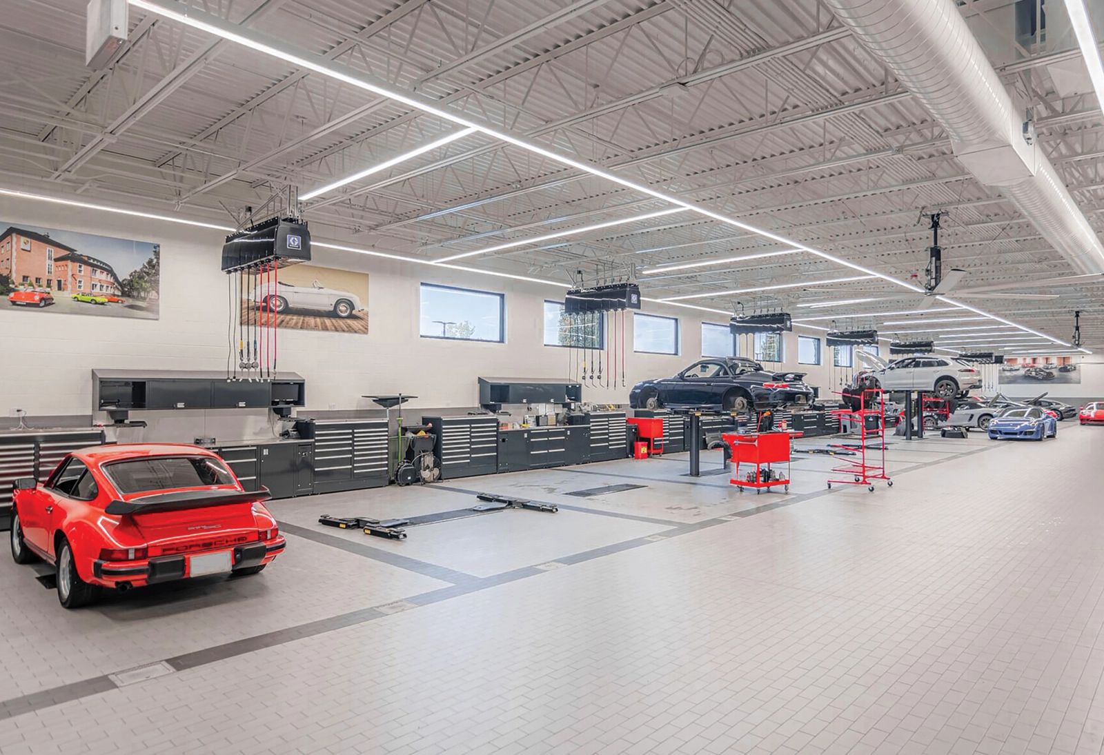 Bright dealership service bay with a red classic sports car and rows of steel workbenches and tool storage along the wall