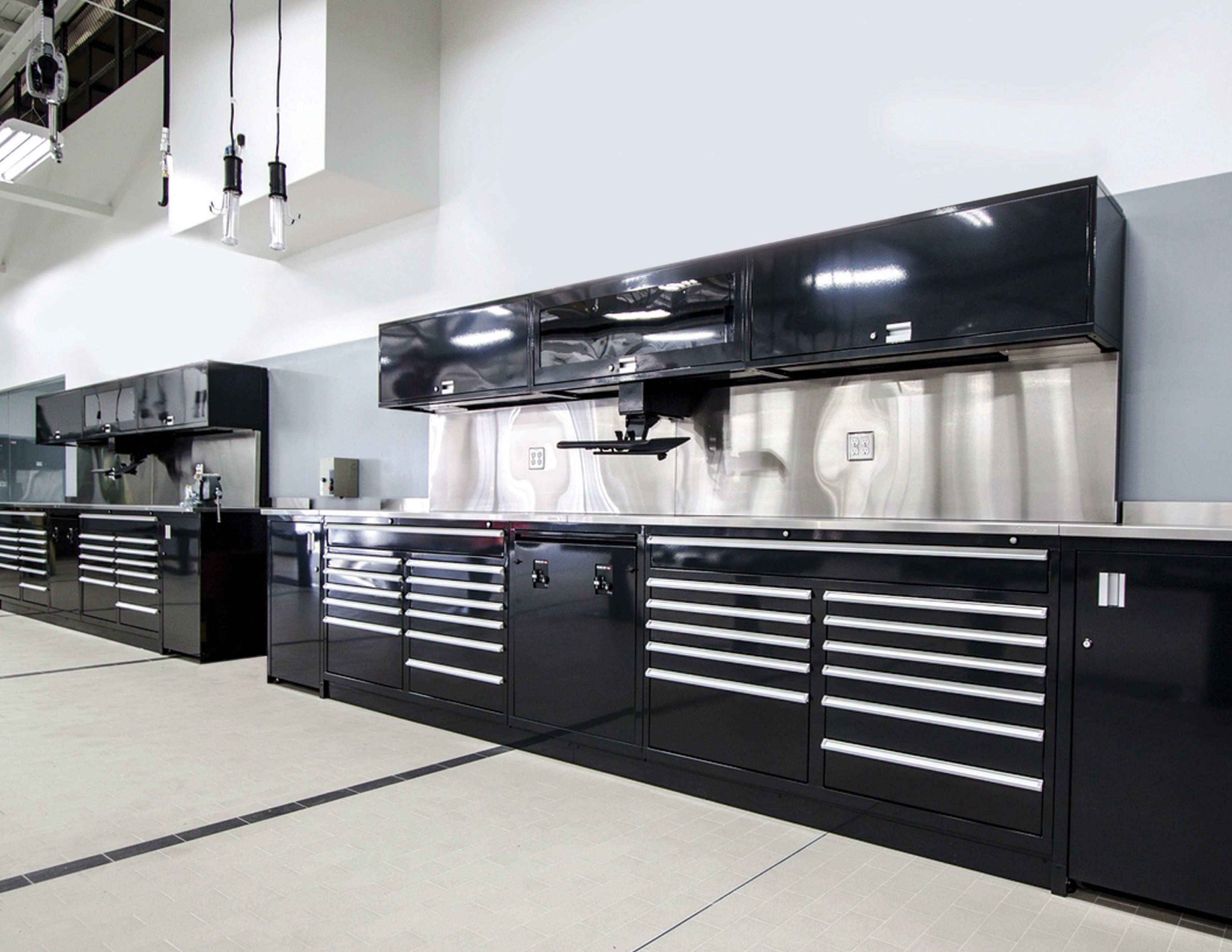 Black powder-coated workbenches with drawers and glossy black upper cabinets in a modern shop