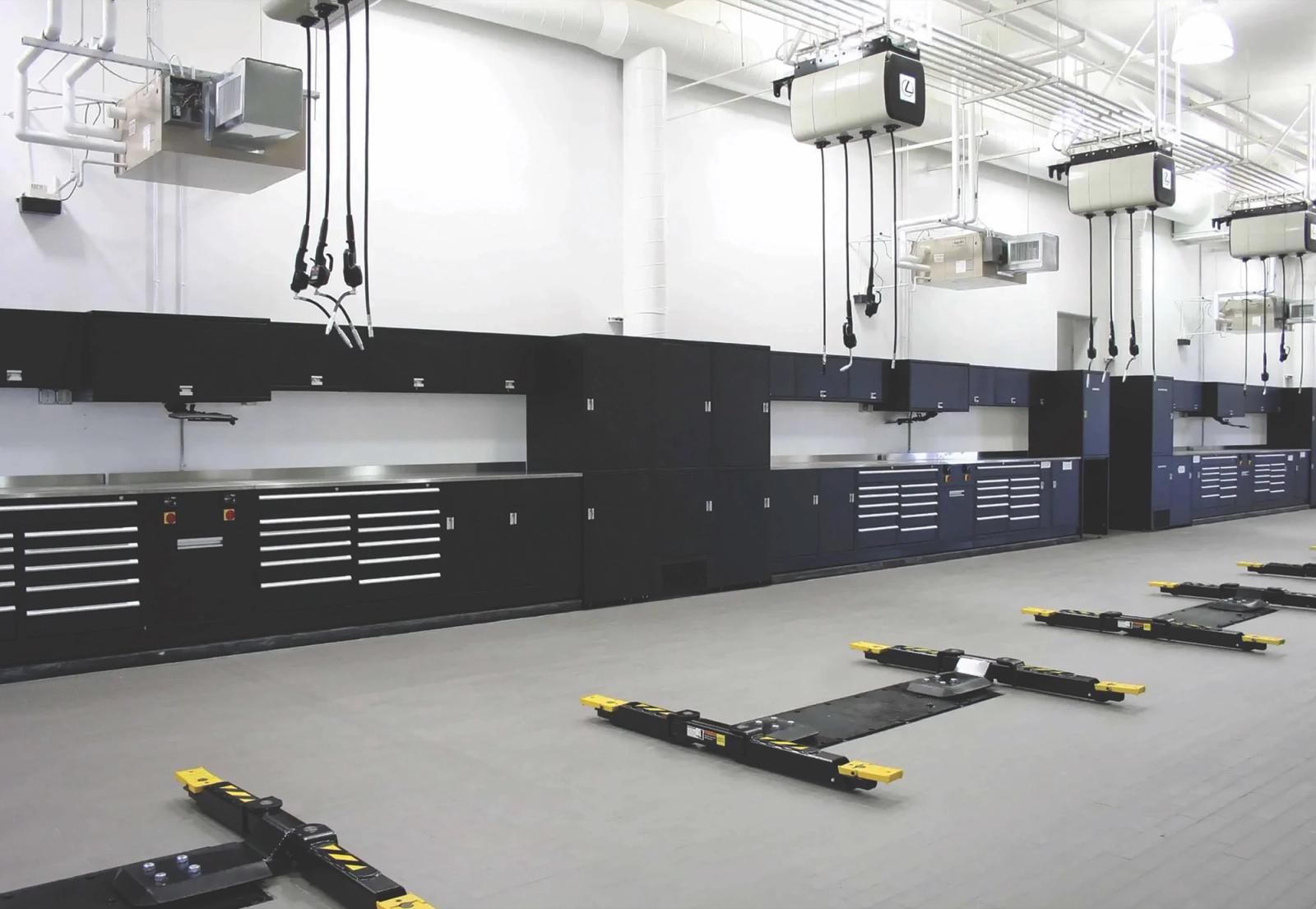 Service shop with black workbenches and tool storage along the wall, overhead reels and yellow lift arms on the floor