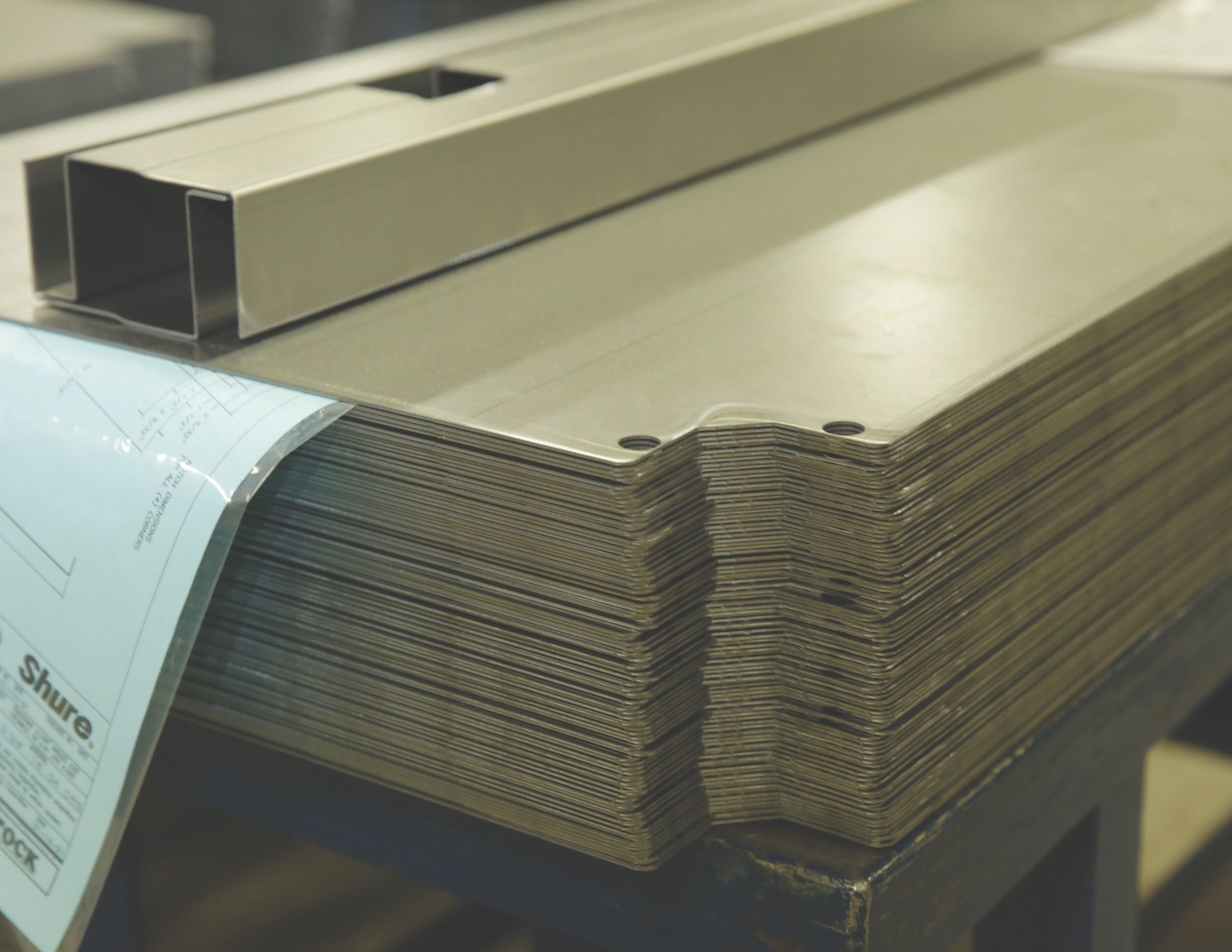 Stack of formed sheet-steel parts with a Shure shop drawing on top