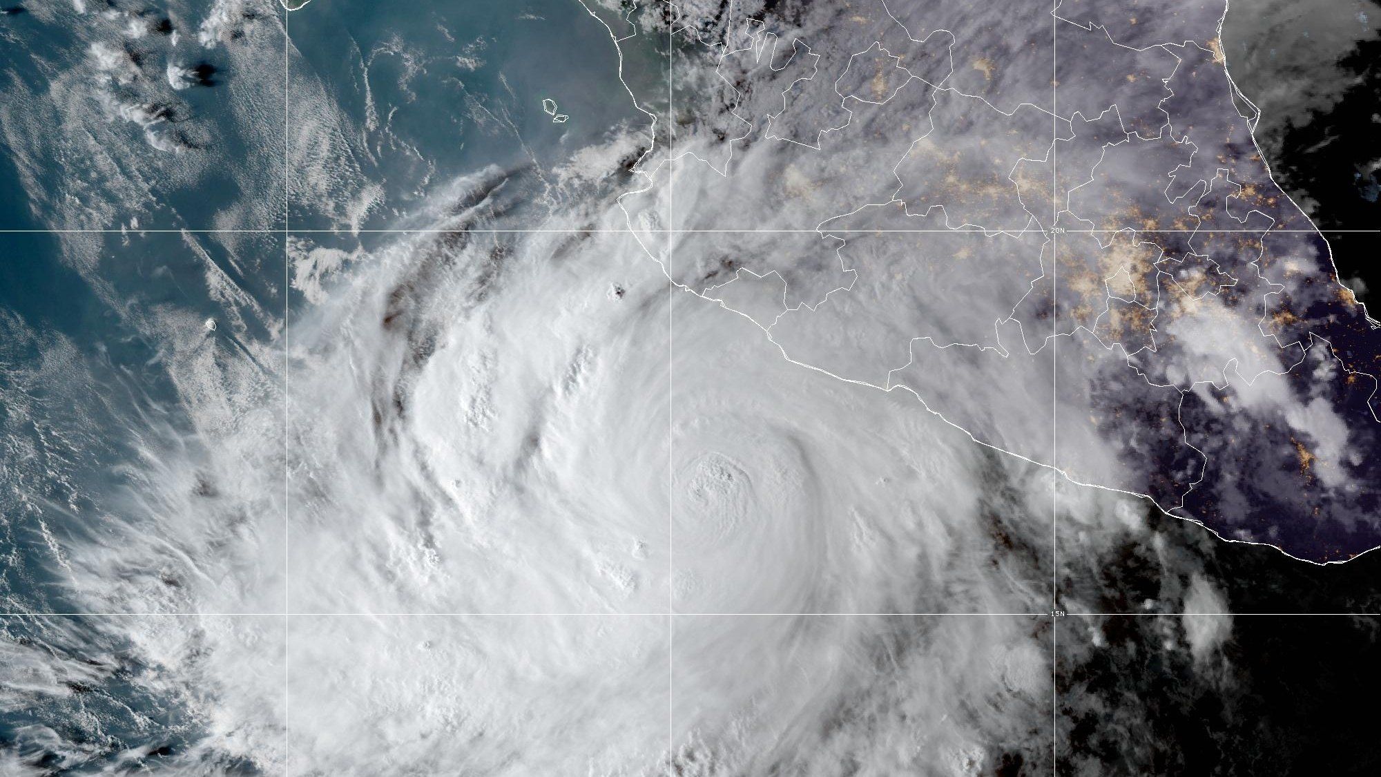 Imagen de satélite en color natural del huracán Simón, un remolino de nubes blancas con el ojo visible frente a la costa del Pacífico mexicano; arriba a la derecha se ven el litoral de Colima, Michoacán y Guerrero y luces de ciudades.