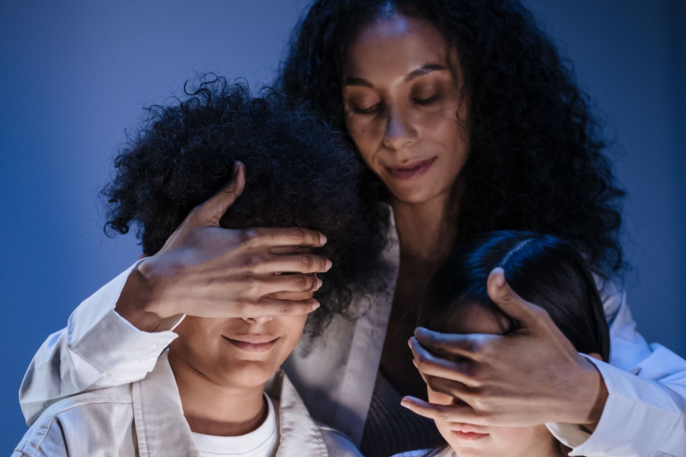 Madre cubre los ojos de dos niños que miran una tablet encendida.
