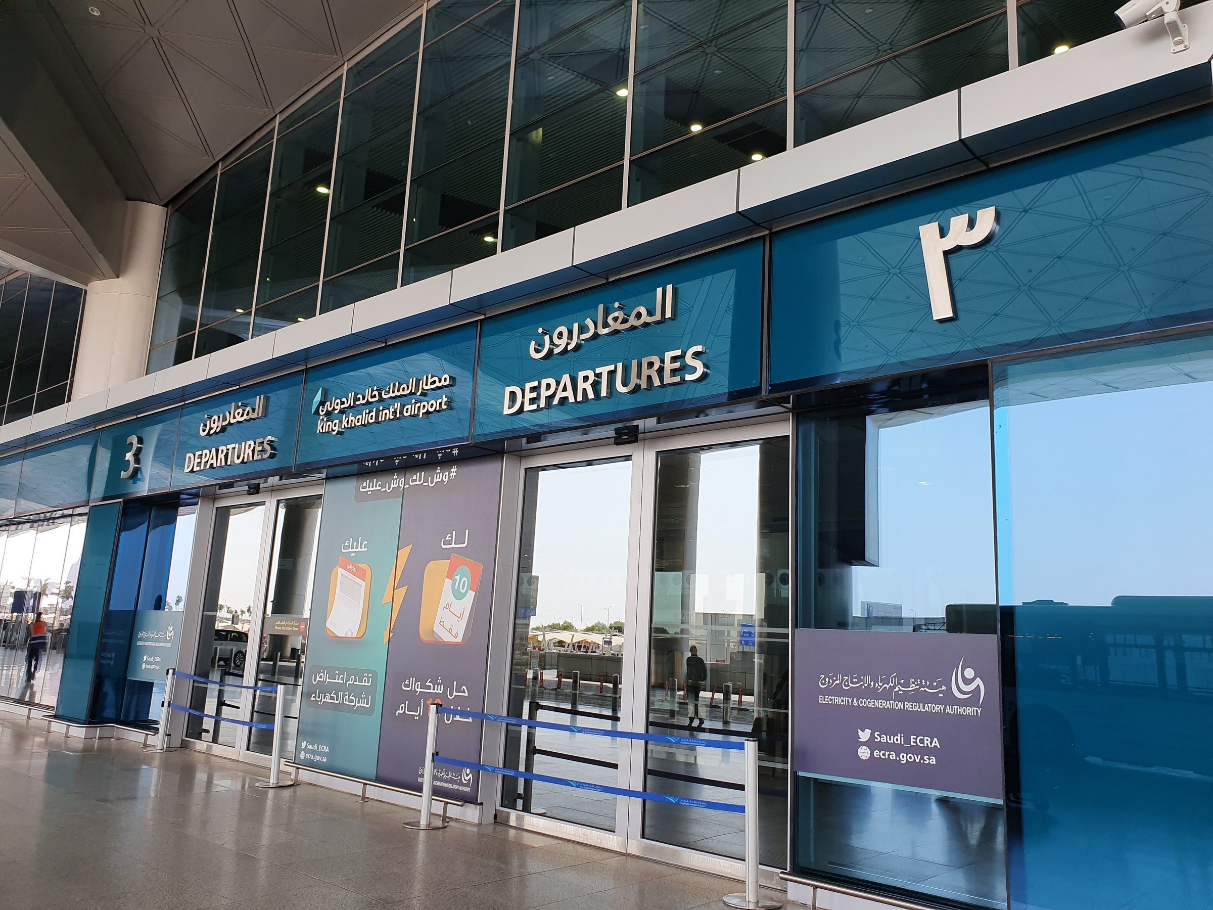 Mostradores de salidas domésticas en el Aeropuerto Internacional Rey Khalid de Riad, con pantallas de vuelos y pasajeros en la sala.
