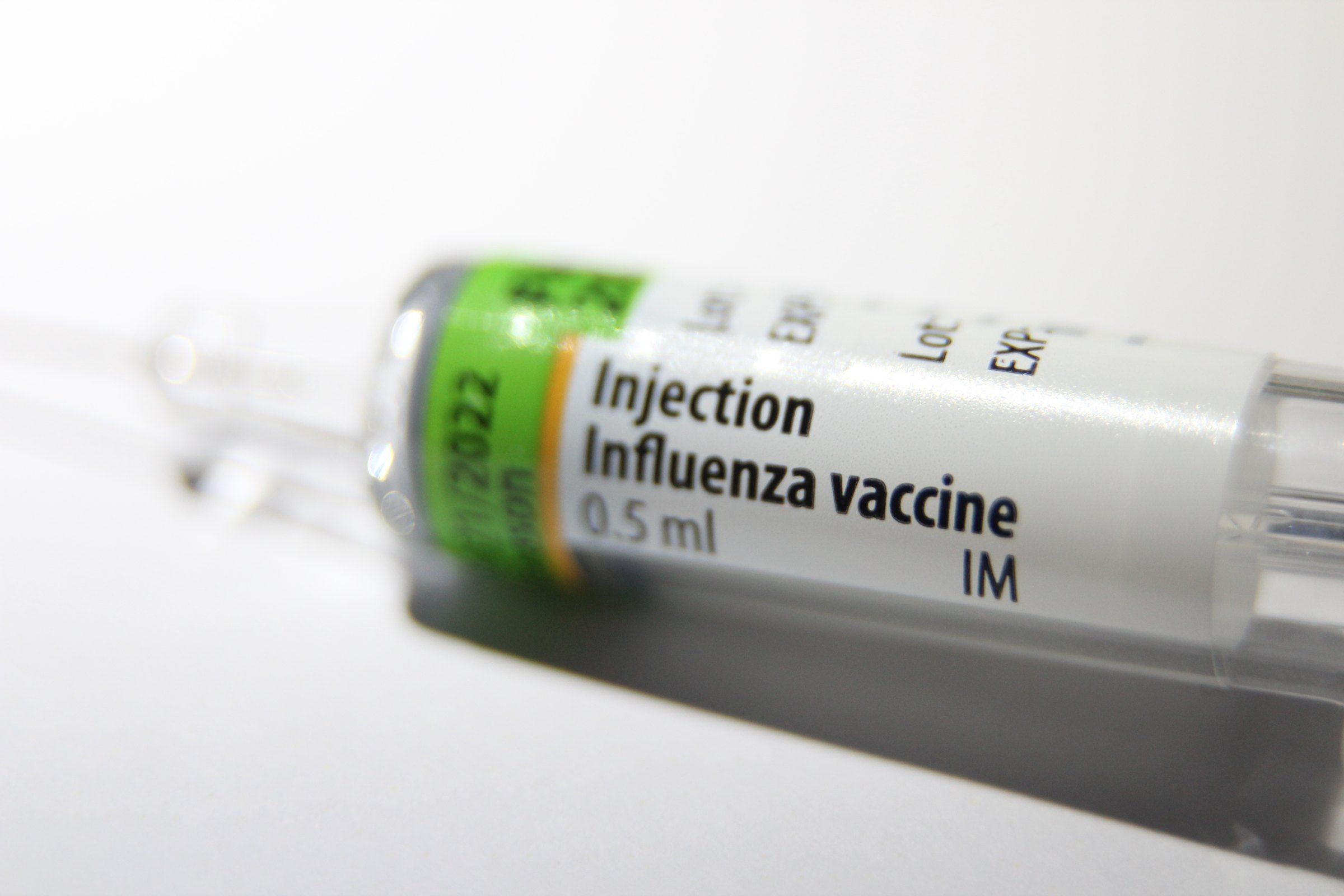 Primer plano de una jeringa prellenada con la etiqueta «Influenza vaccine 0.5 ml IM» sobre un fondo blanco.