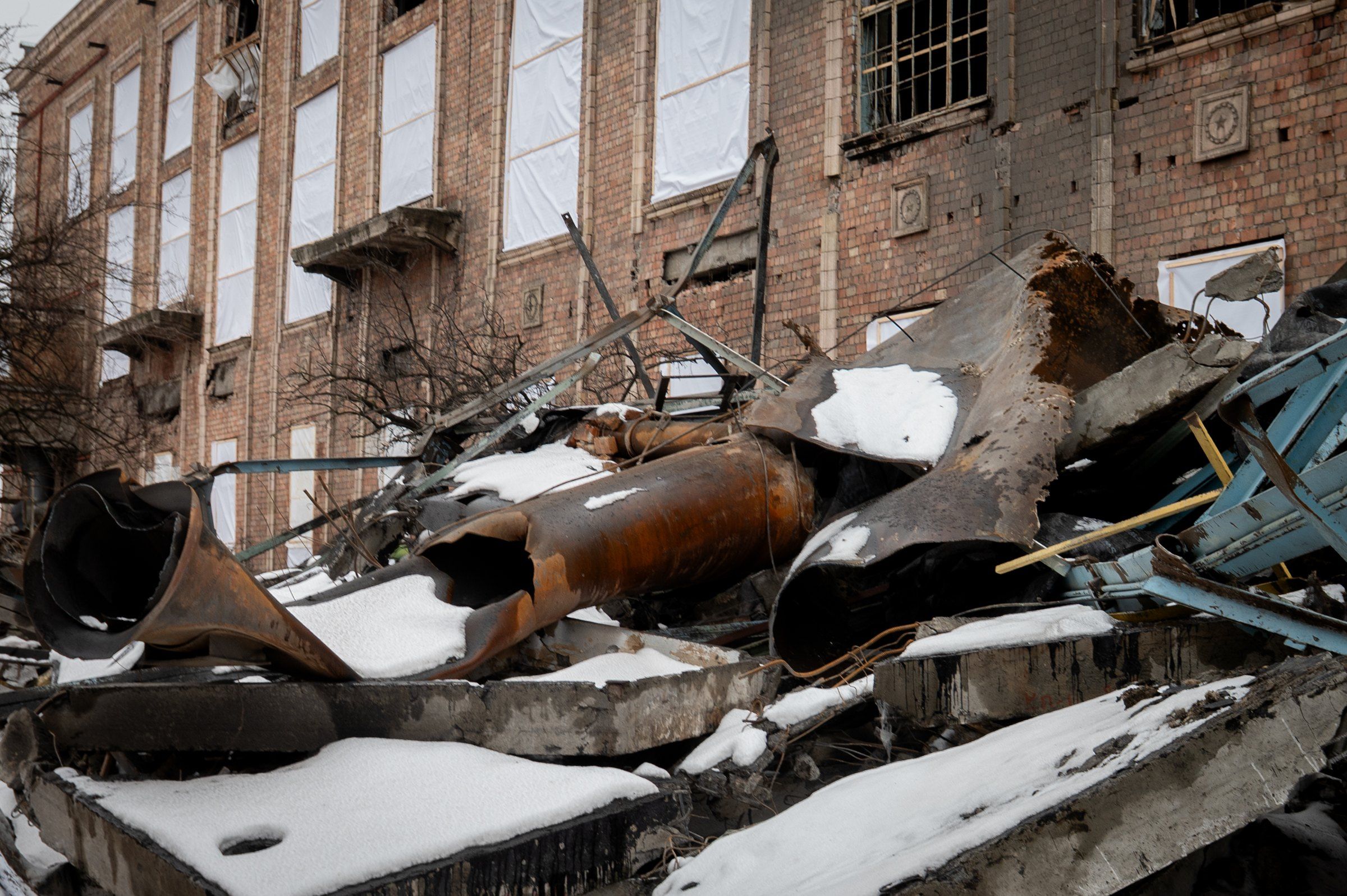Restos retorcidos de tuberías y estructuras metálicas cubiertos de nieve frente al edificio de ladrillo dañado de la central termoeléctrica de Darnytsia, en Kiev, con ventanas tapadas con plástico.