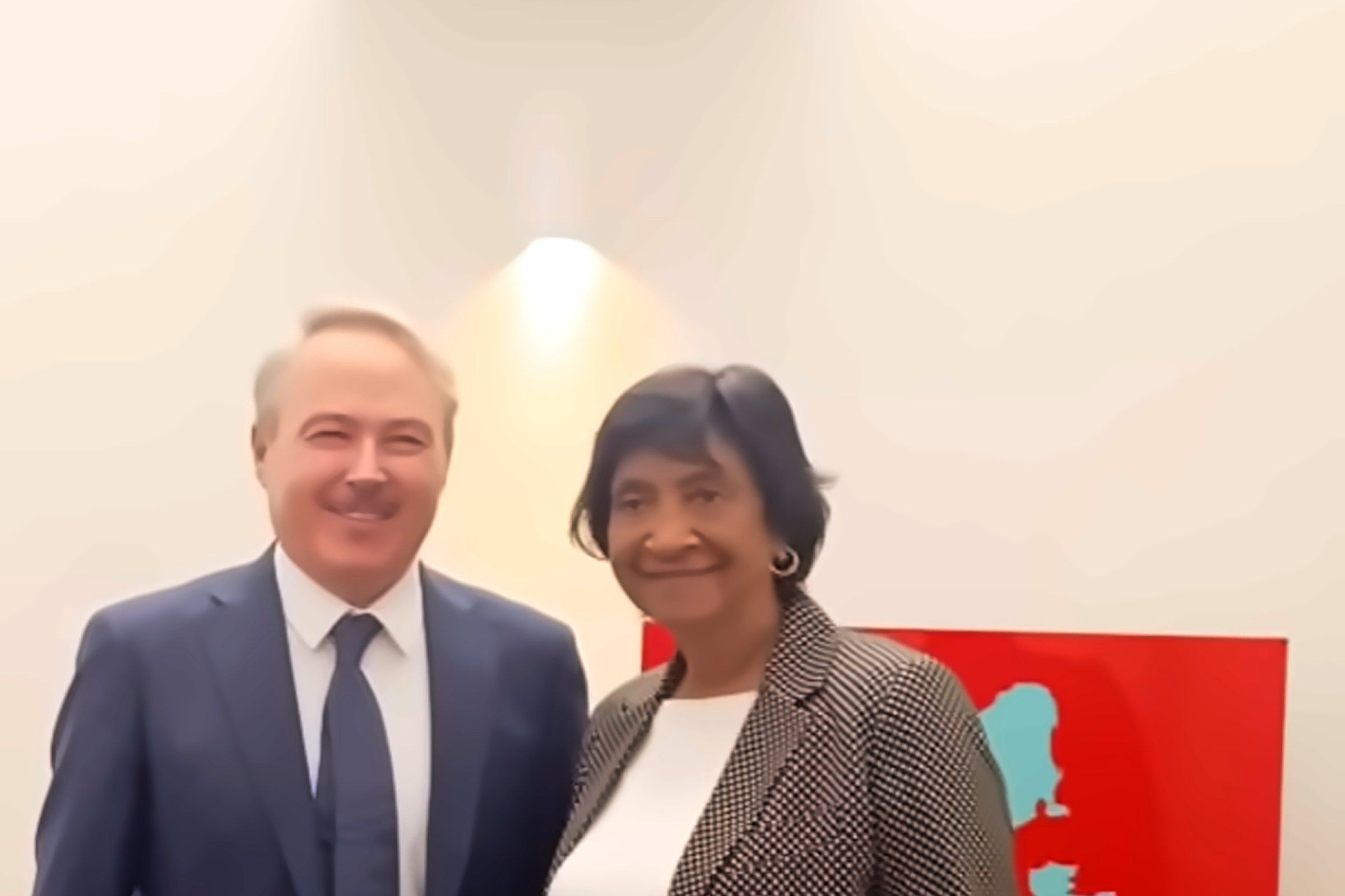 Navi Pillay, con saco de pata de gallo y blusa blanca, sonríe junto al pintor Arrigo Musti frente a un muro claro y un cuadro rojo en el edificio de los Juicios de Núremberg.