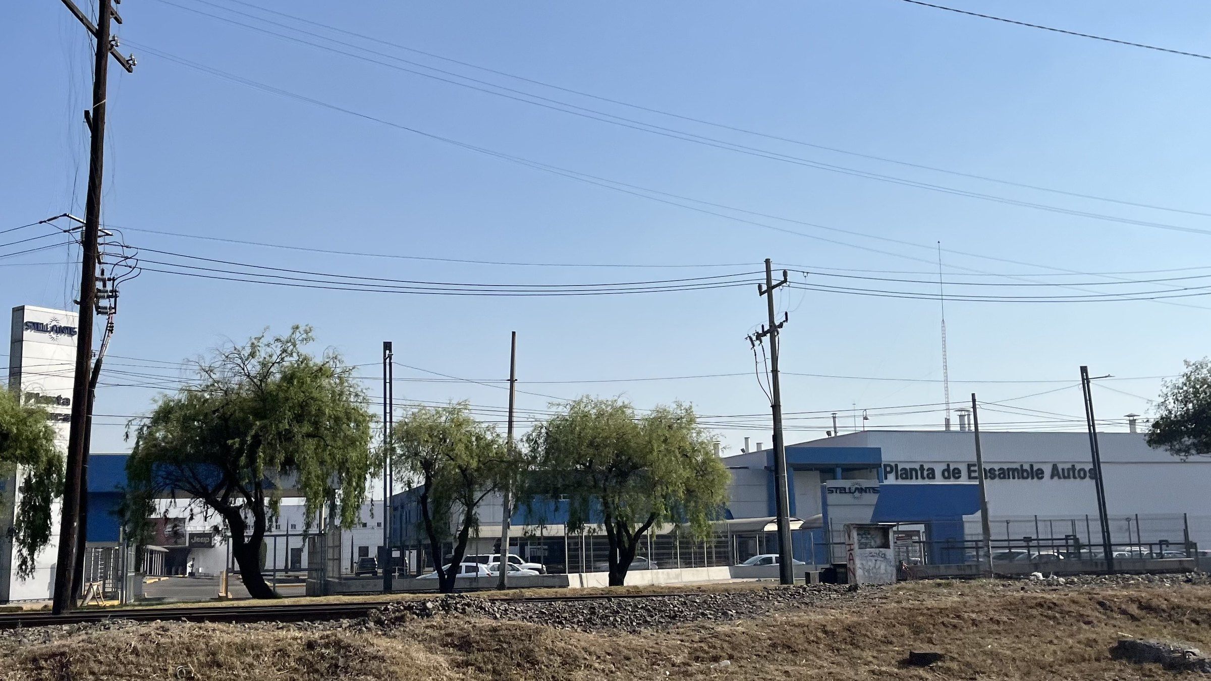 Planta de ensamble de autos de Stellantis en Toluca, con el letrero «Planta de Ensamble Autos», árboles y postes de luz al frente.