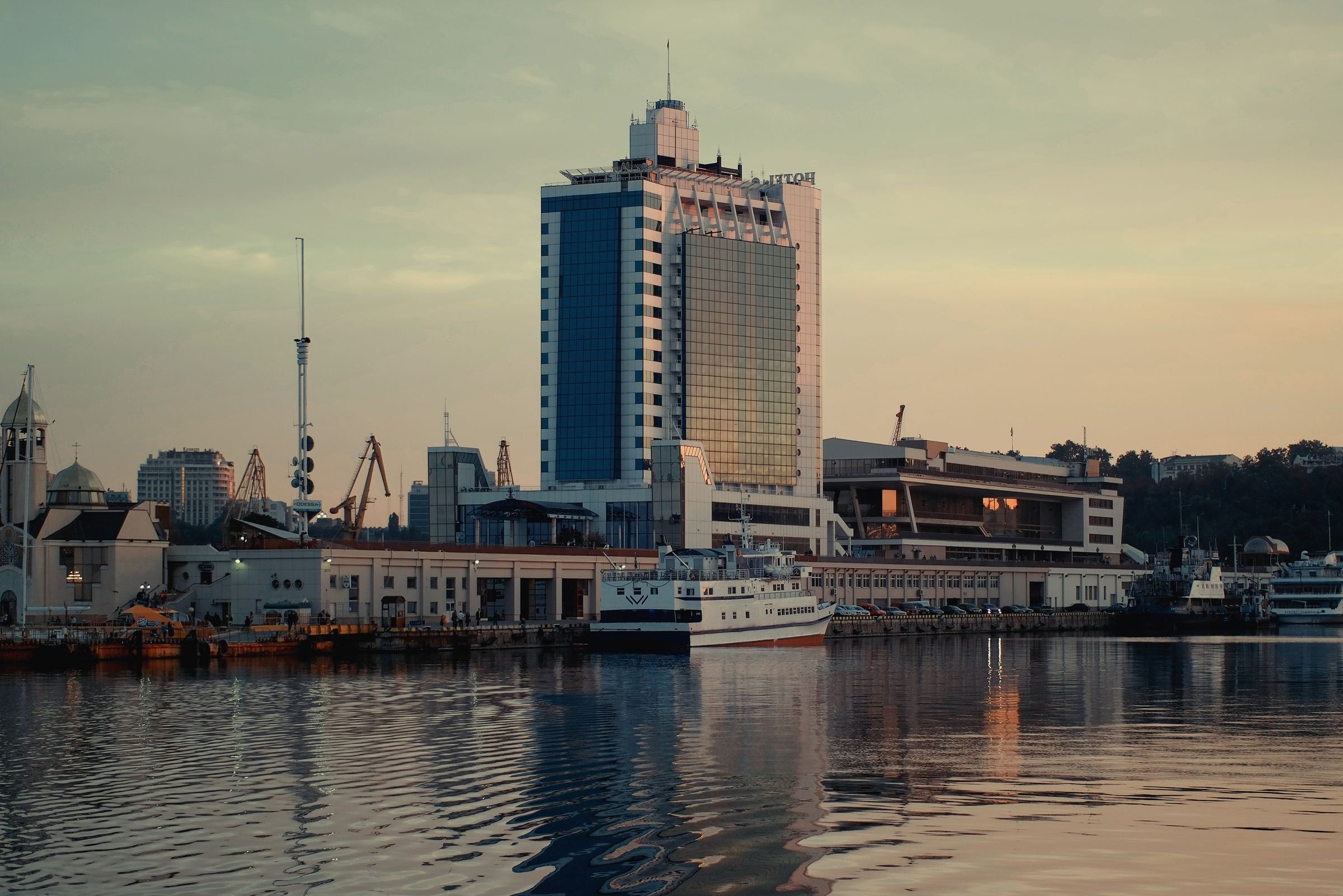 Vista del puerto de Odesa, en Ucrania, con muelles, edificios y embarcaciones al atardecer.