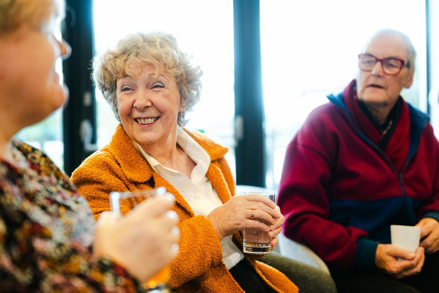 Drie ouderen in gesprek aan een tafel, met een kopje koffie
