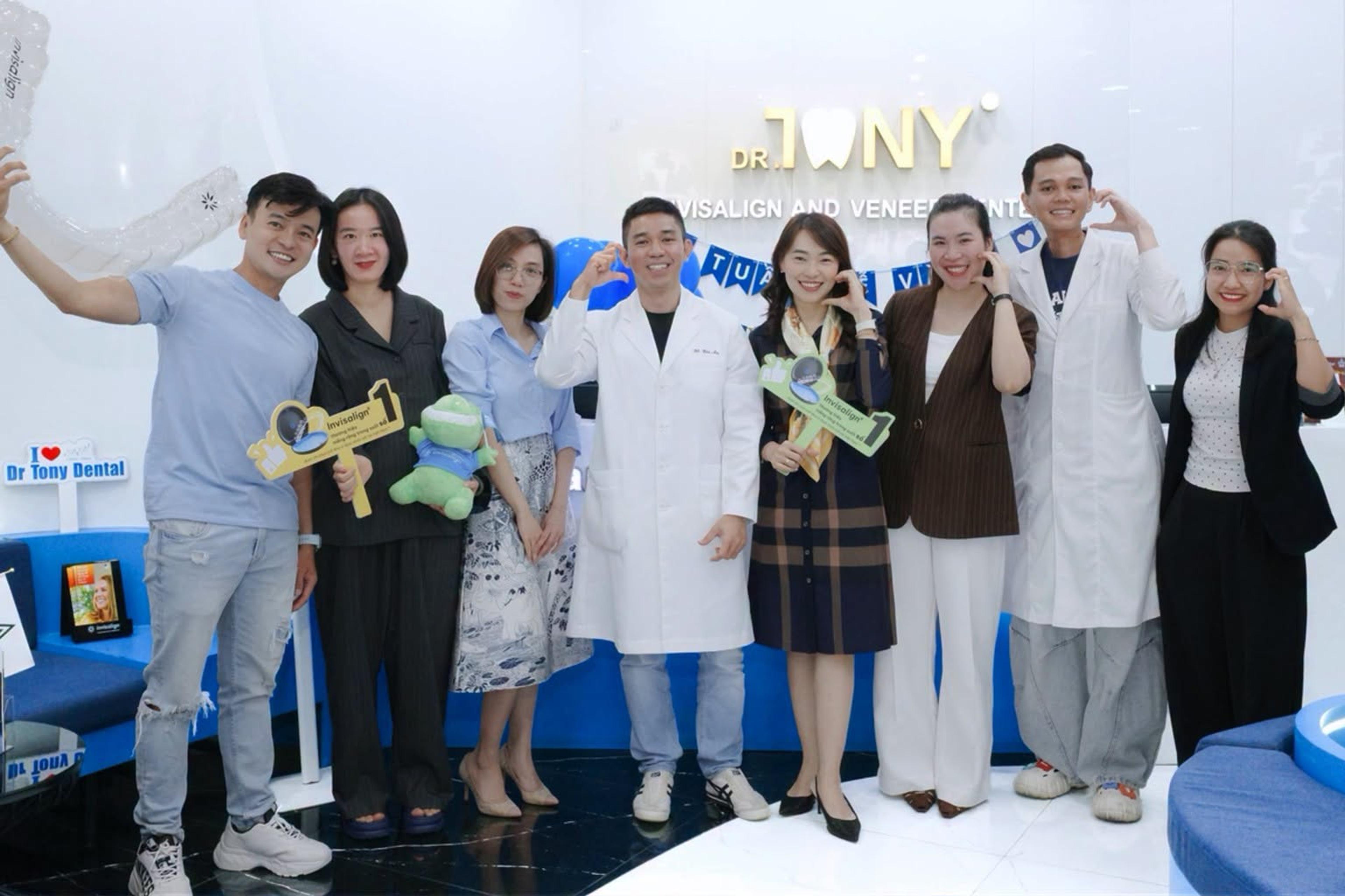 Đội ngũ Dr Tony Dental cùng khách mời cầm bảng cổ vũ Invisalign chụp chung tại khu chờ của phòng khám.