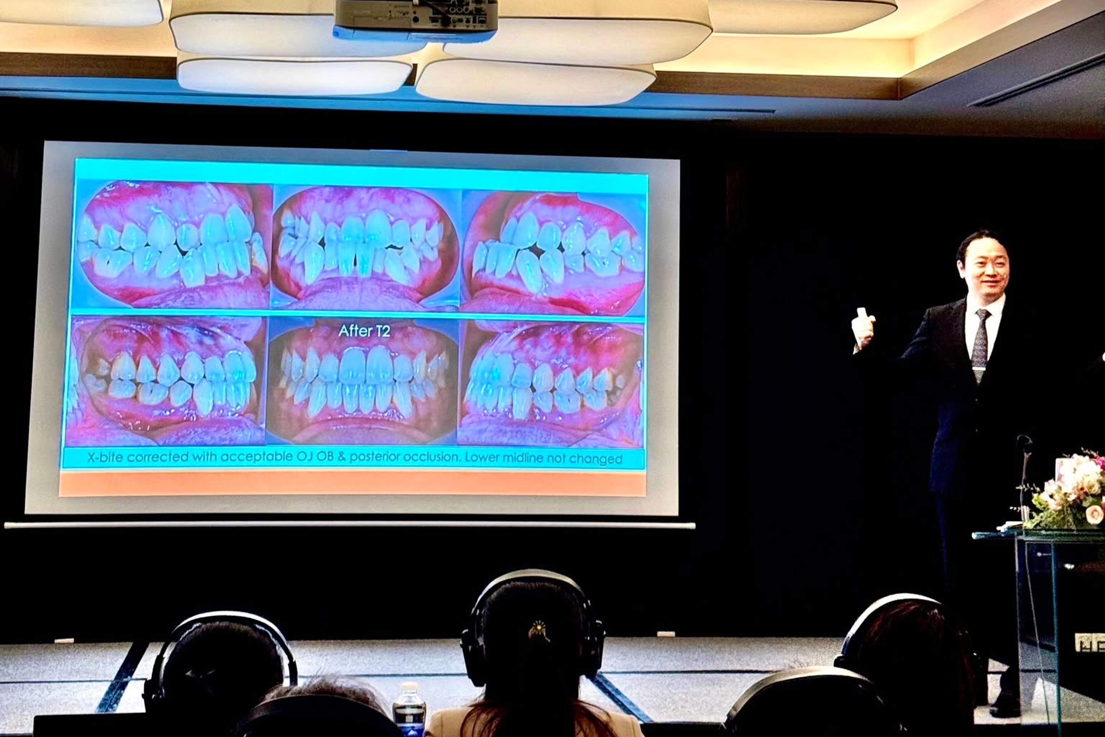 Bác sĩ Yau Yi Kwong trình bày một ca lâm sàng trên màn chiếu trong hội trường; học viên ngồi nghe với tai nghe phiên dịch.