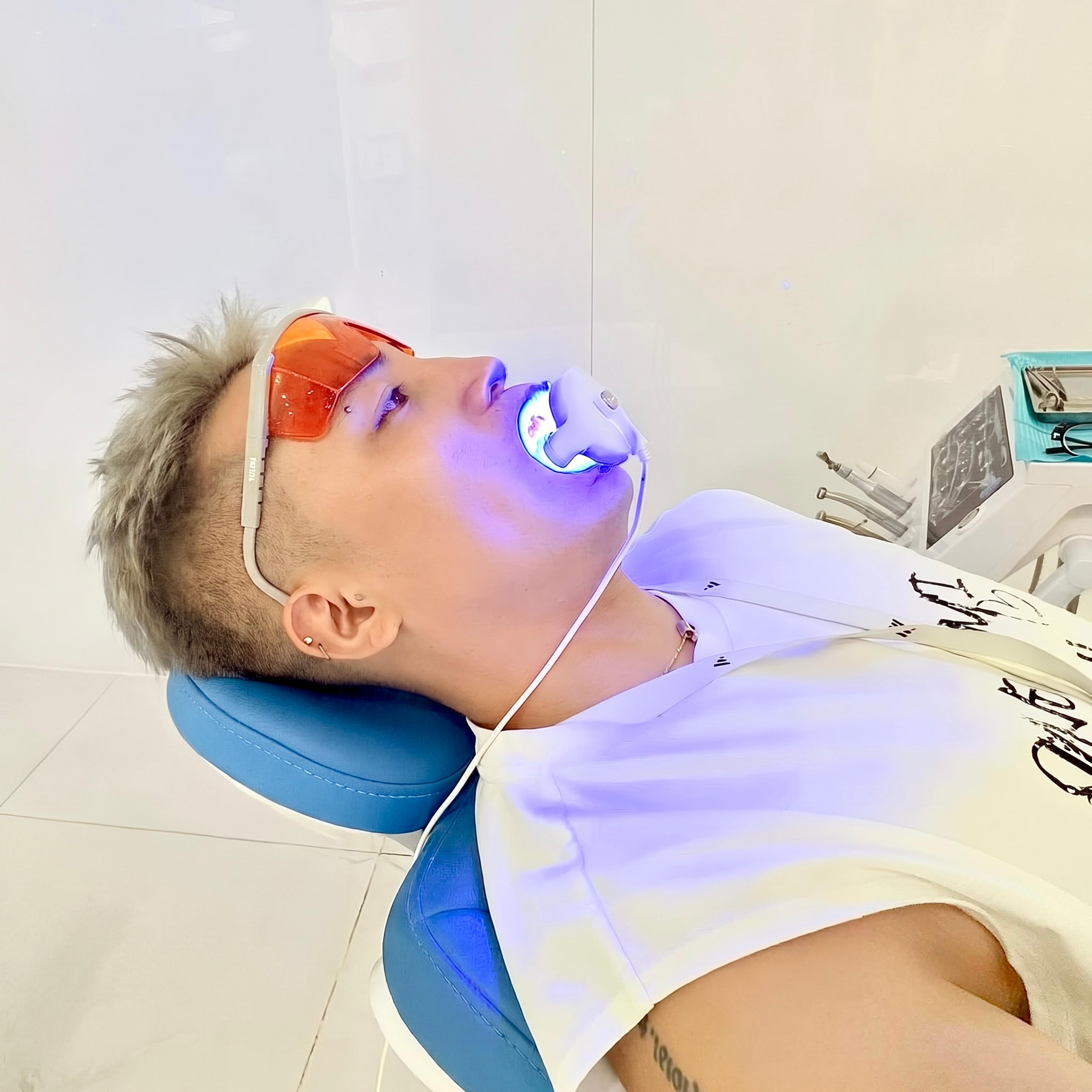 Khách hàng đeo kính bảo hộ màu cam, ngả trên ghế nha khoa trong lúc chiếu đèn tẩy trắng