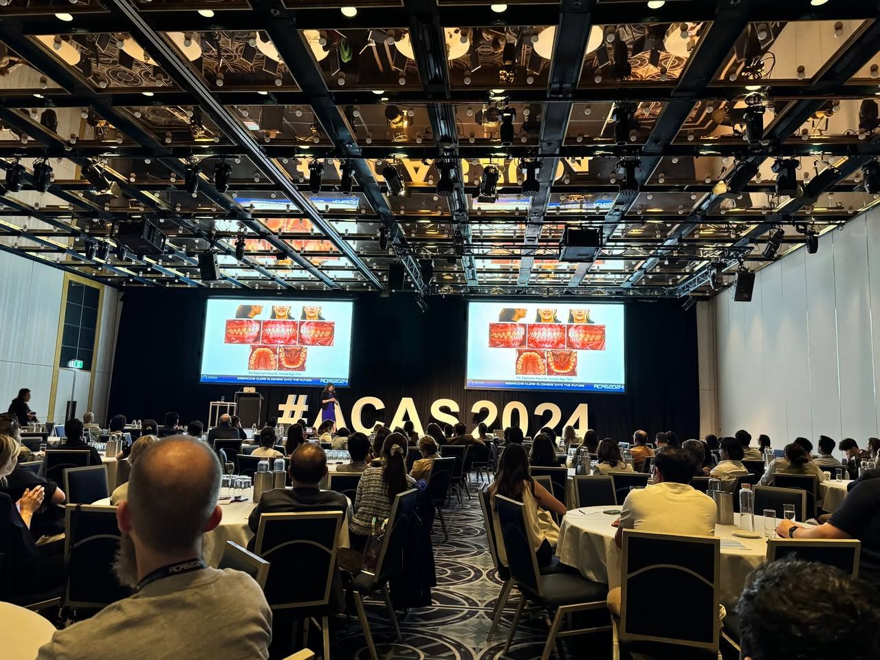 Toàn cảnh hội trường ACAS 2024 với hai màn chiếu lớn và dãy chữ “#ACAS2024” trên sân khấu, đại biểu ngồi kín các bàn phía dưới.