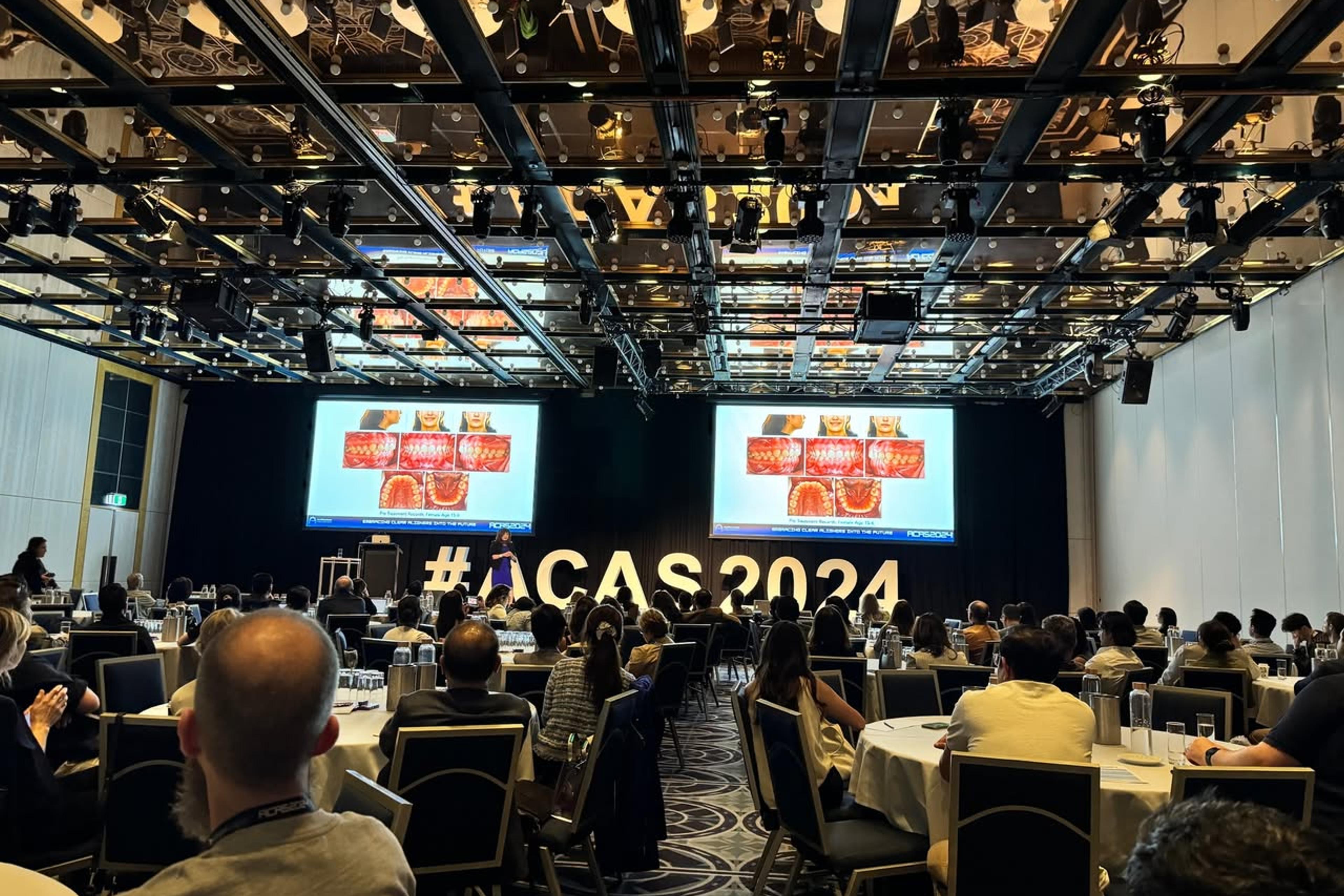 Toàn cảnh hội trường ACAS 2024 với hai màn chiếu lớn và dãy chữ “#ACAS2024” trên sân khấu, đại biểu ngồi kín các bàn phía dưới.