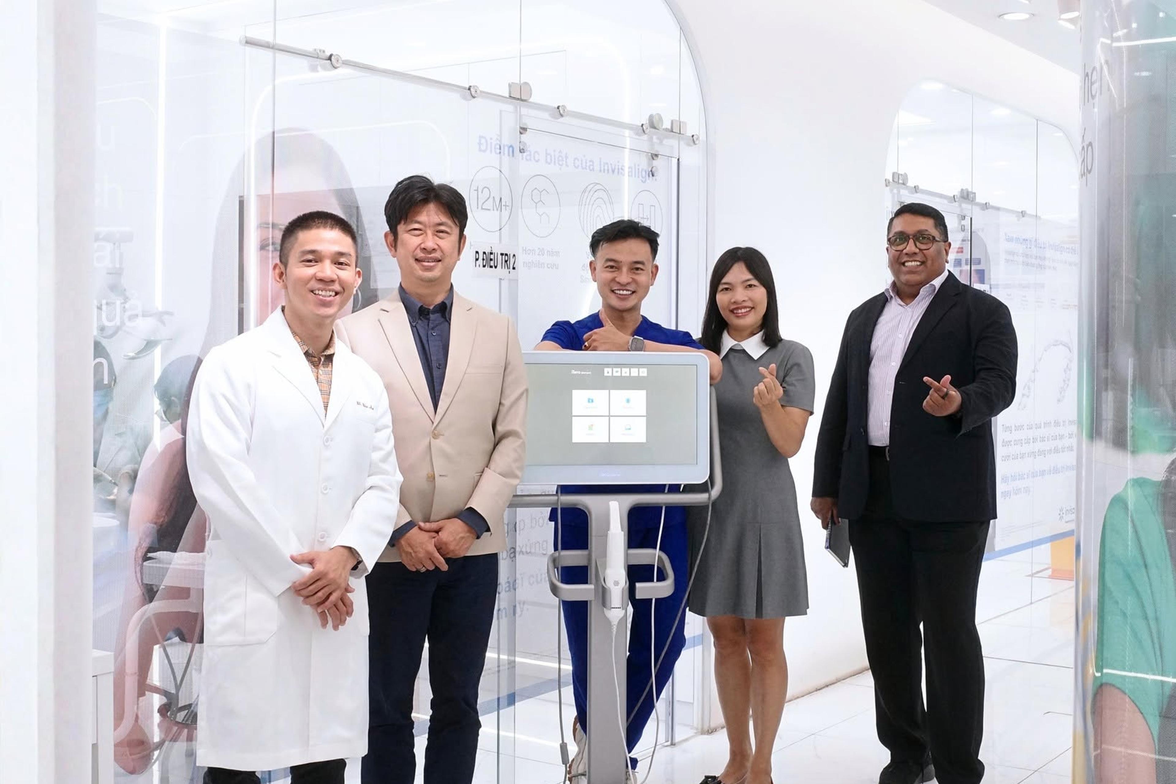 Năm người đứng cạnh máy quét trong phòng điều trị của Dr Tony Dental; dải chữ dưới ảnh ghi “Dr Tony Dental hân hạnh đón tiếp Mr. Takashi & Mr. Sandeep — Giám đốc khu vực Đông Nam Á & Việt Nam, Công ty Align Tech — Invisalign toàn cầu”.