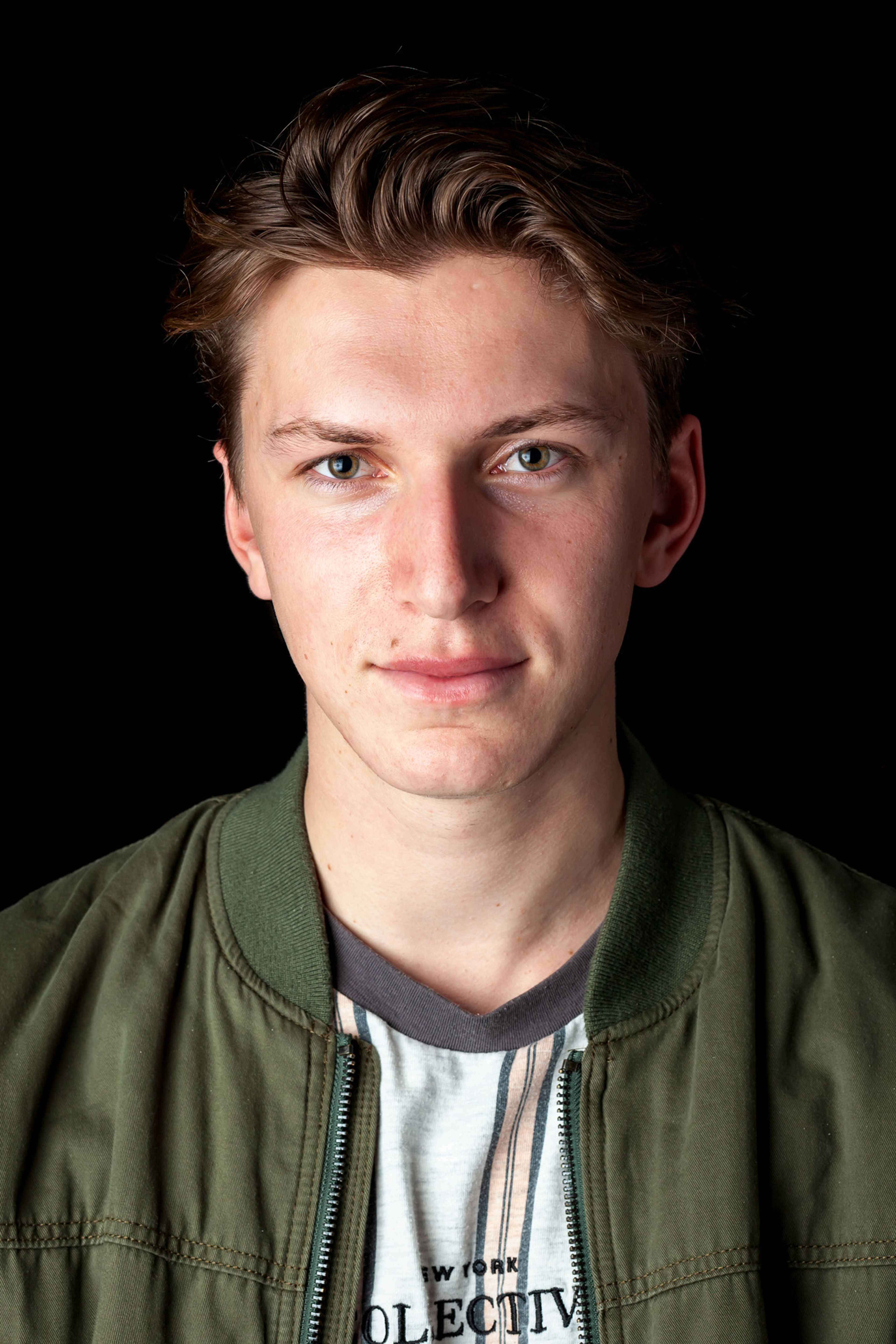 Headshot of a man with short, wavy hair, wearing a green jacket over a graphic T-shirt