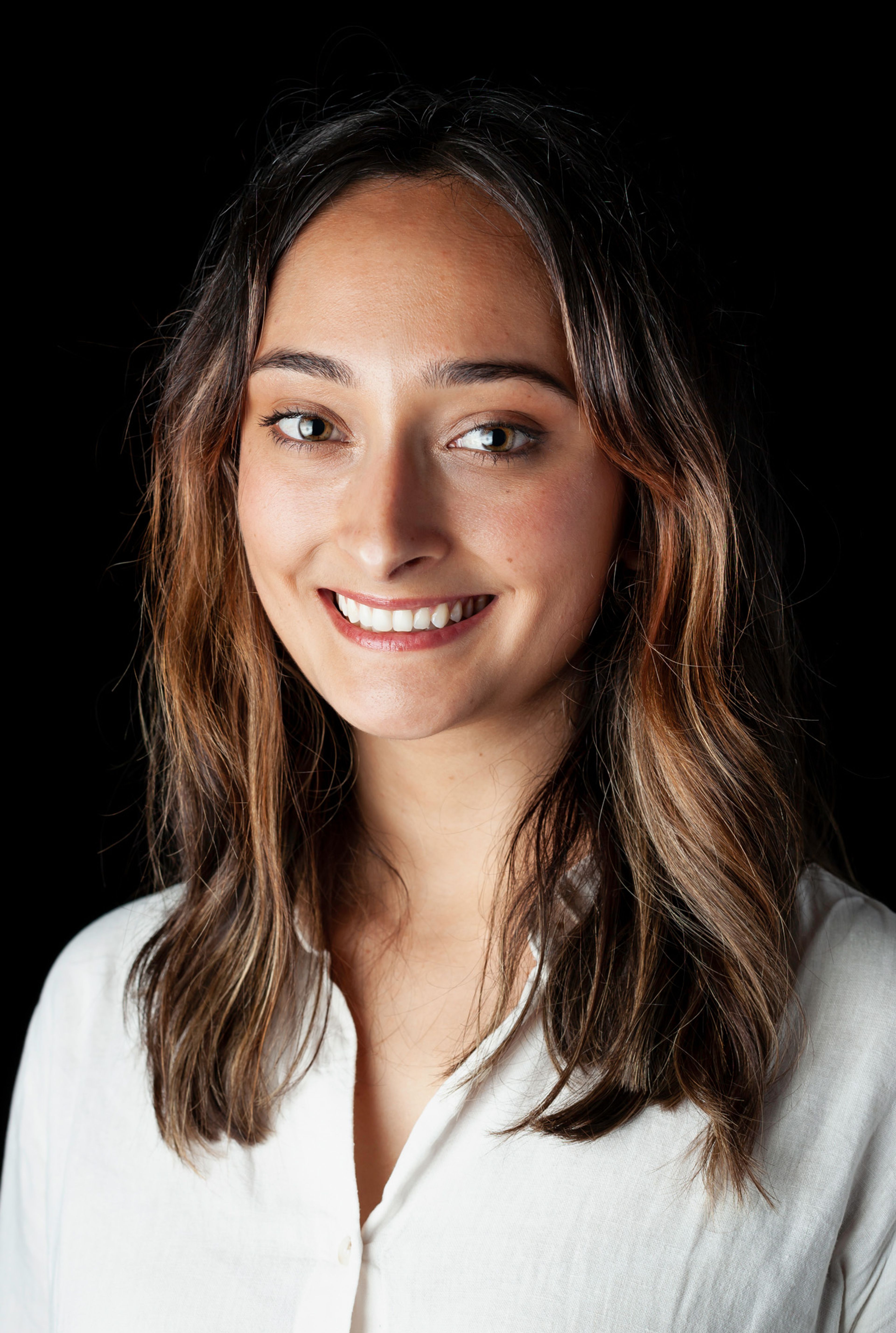 A portrait of a young woman with shoulder-length brown hair, wearing a white button-down shirt