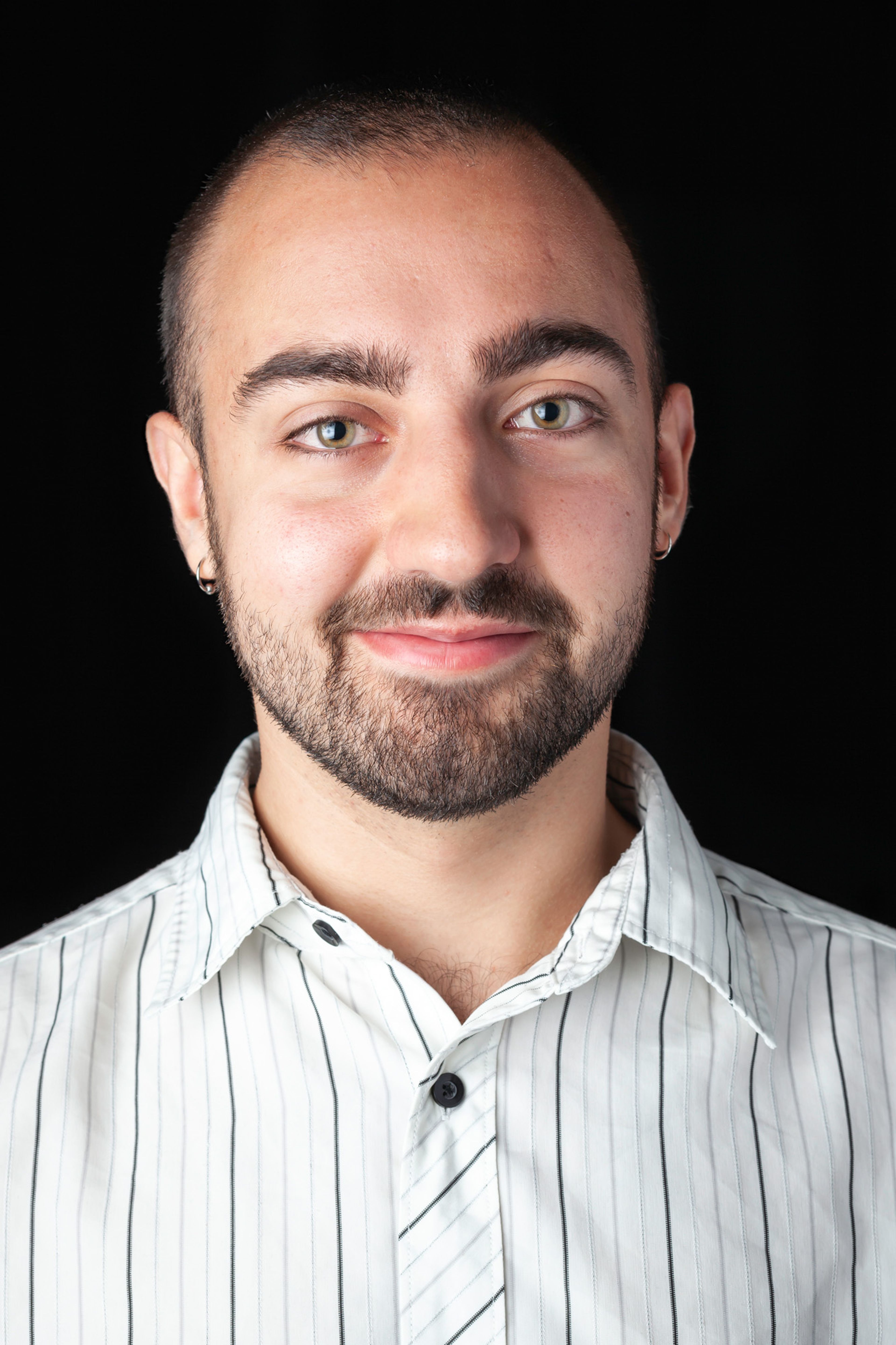 A headshot of a smiling individual with a short beard and a neatly trimmed haircut, wearing a white, pinstriped shirt