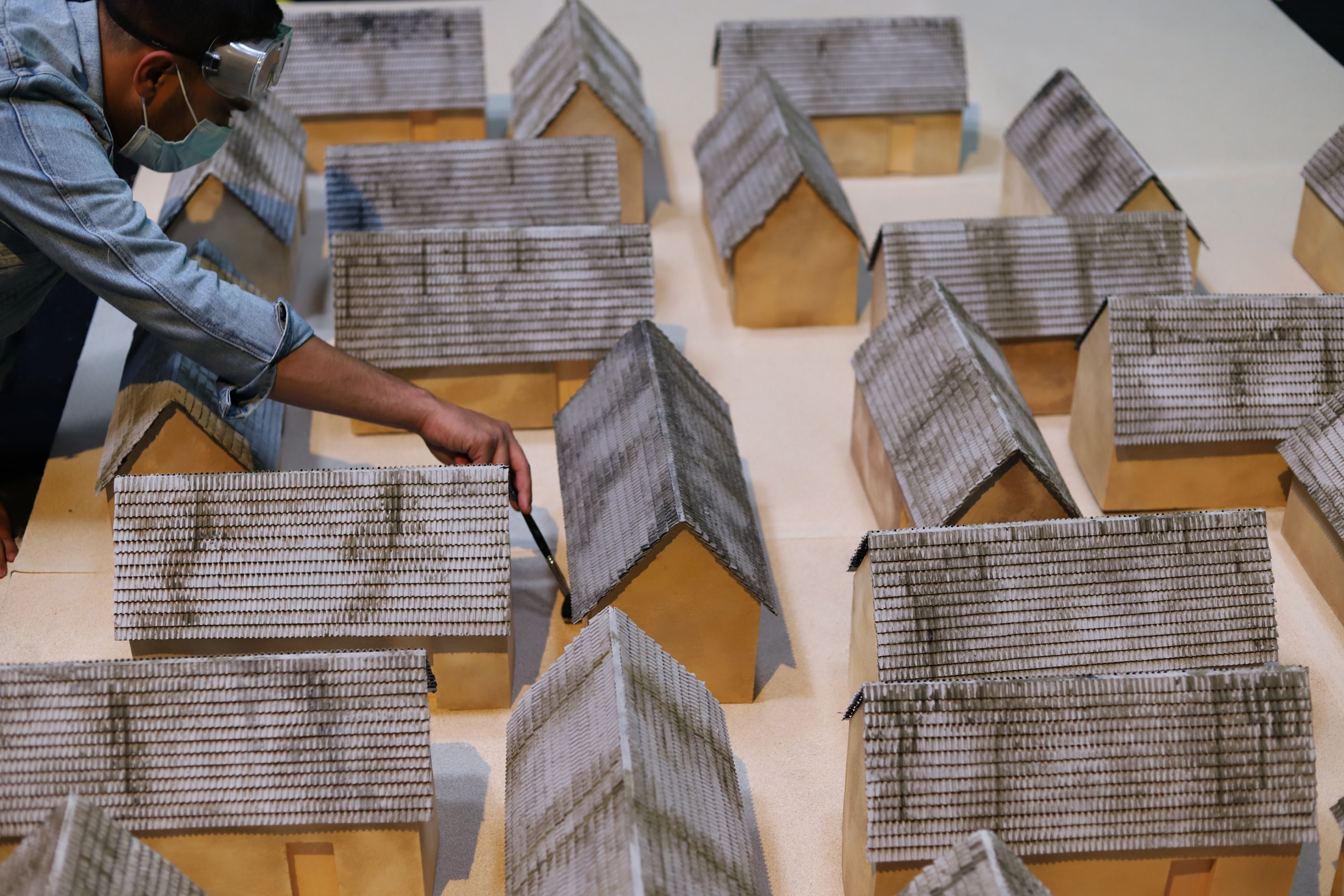 A person working on a detailed model of small houses with shingled roofs, carefully painting one of the structures