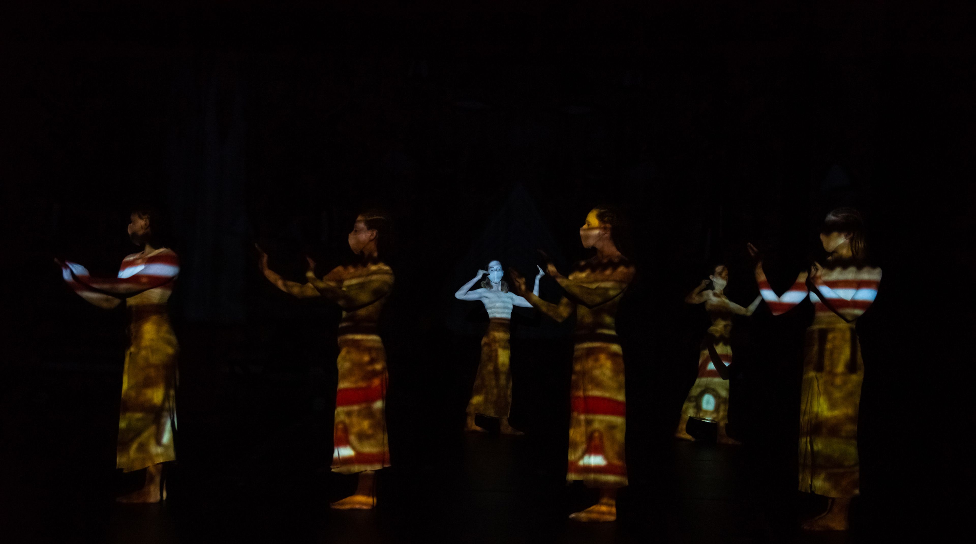 A dance performance with dancers dimly illuminated by colorful, patterned projection