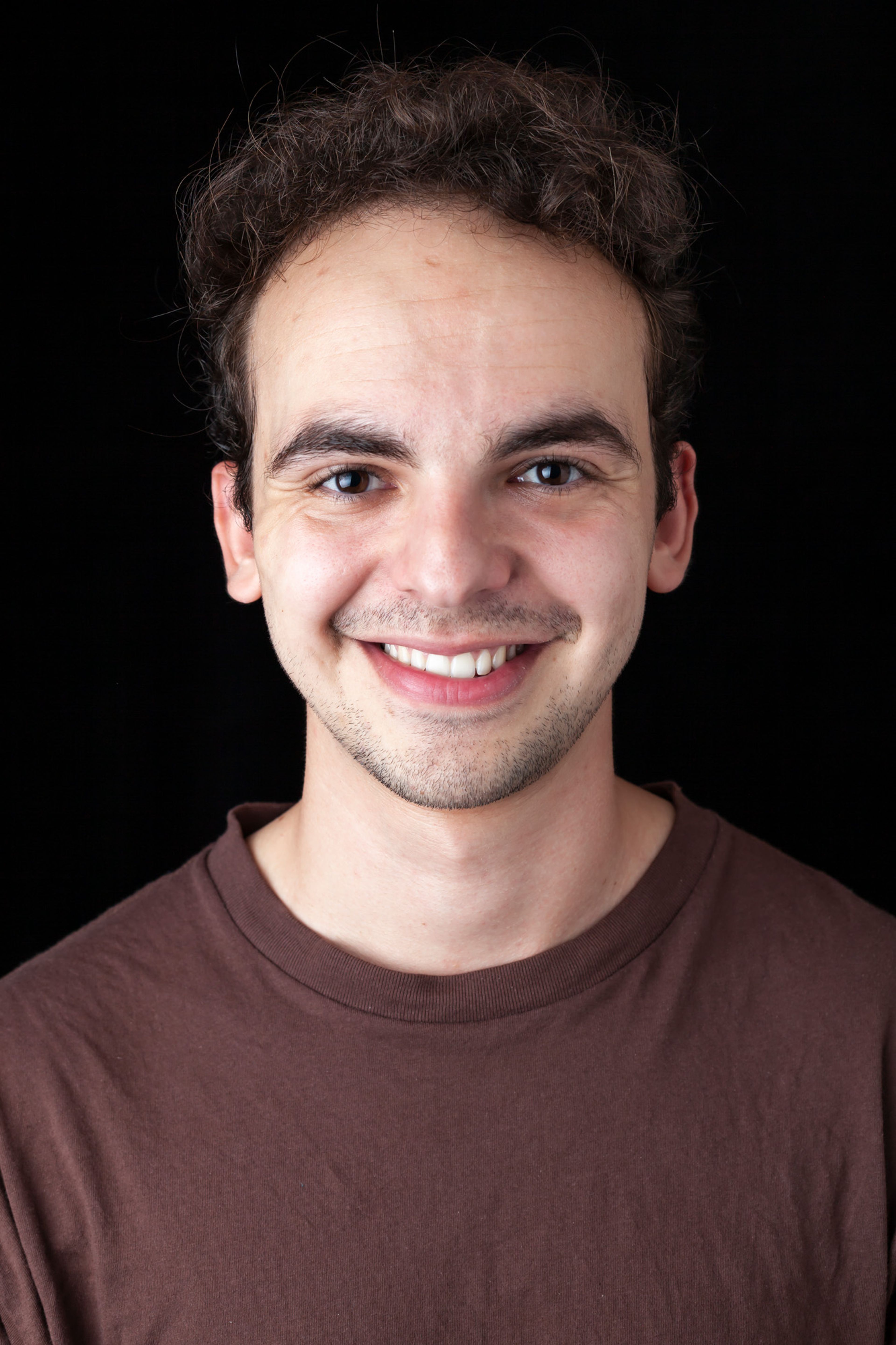 A portrait of a smiling person wearing a brown shirt, with short curly hair