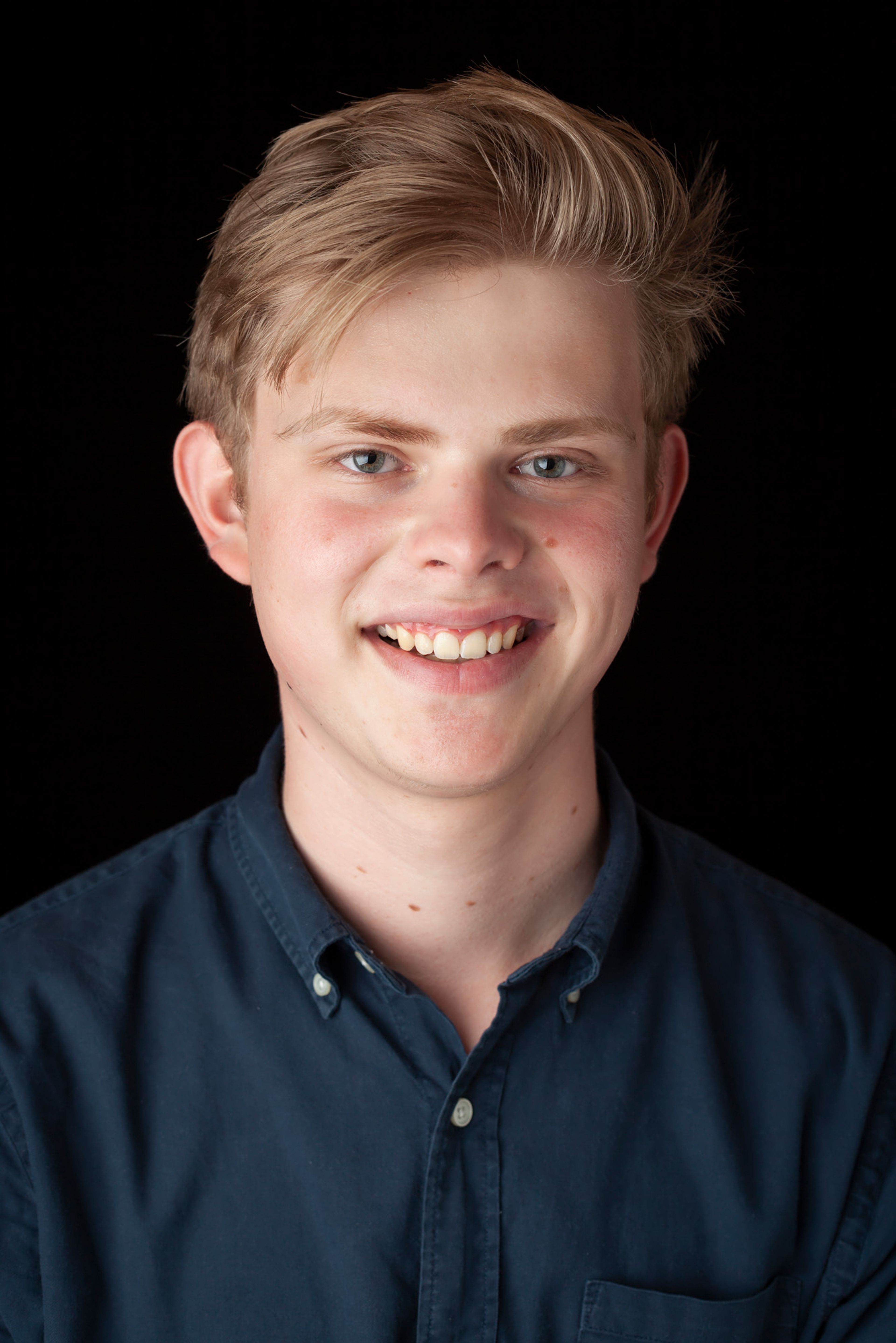 A young man with light hair, smiling, wearing a navy button-up shirt